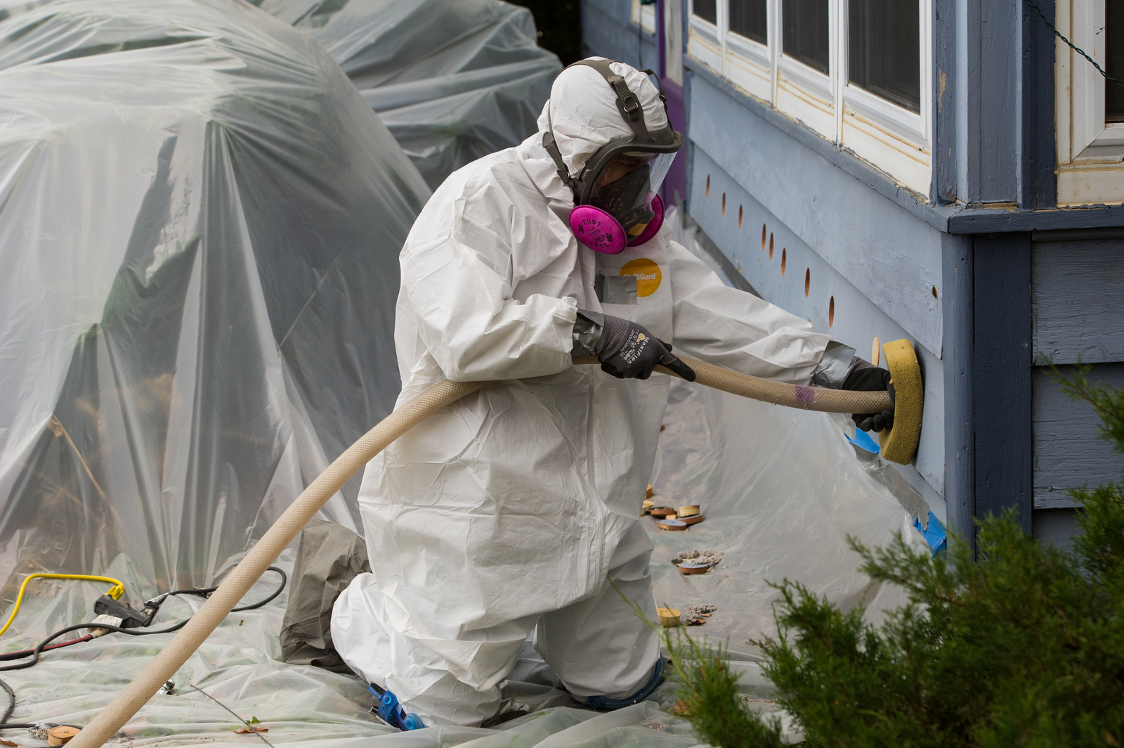 Weatherization worker installs insulation into a house wall.