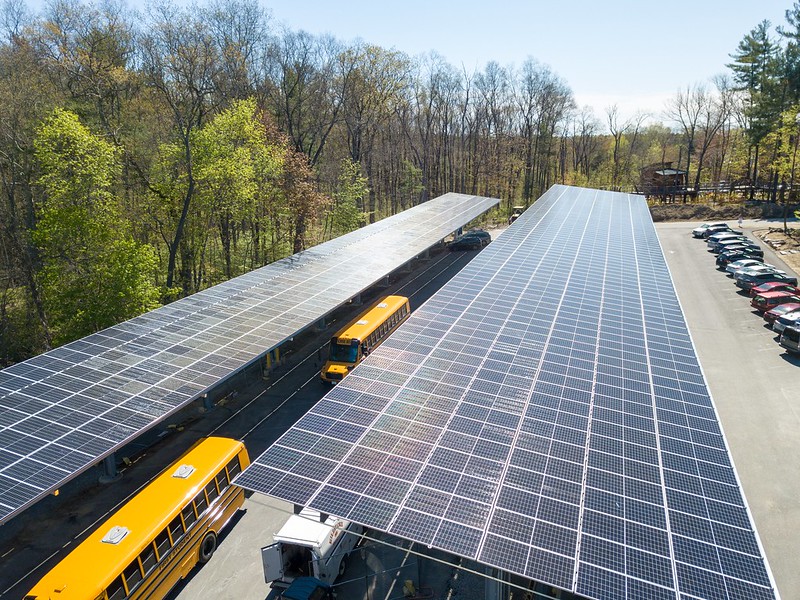 Two school buses drive below community solar arrays