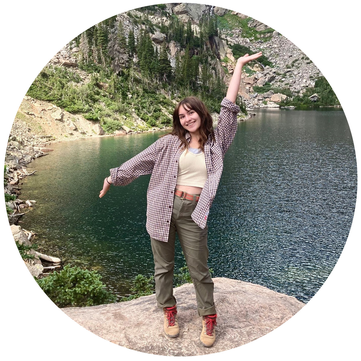 Person standing on rock with lake and rocky mountain in background.