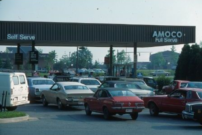 Historical photo of lines of 1960/1970-style cars waiting at a gas station for fuel.