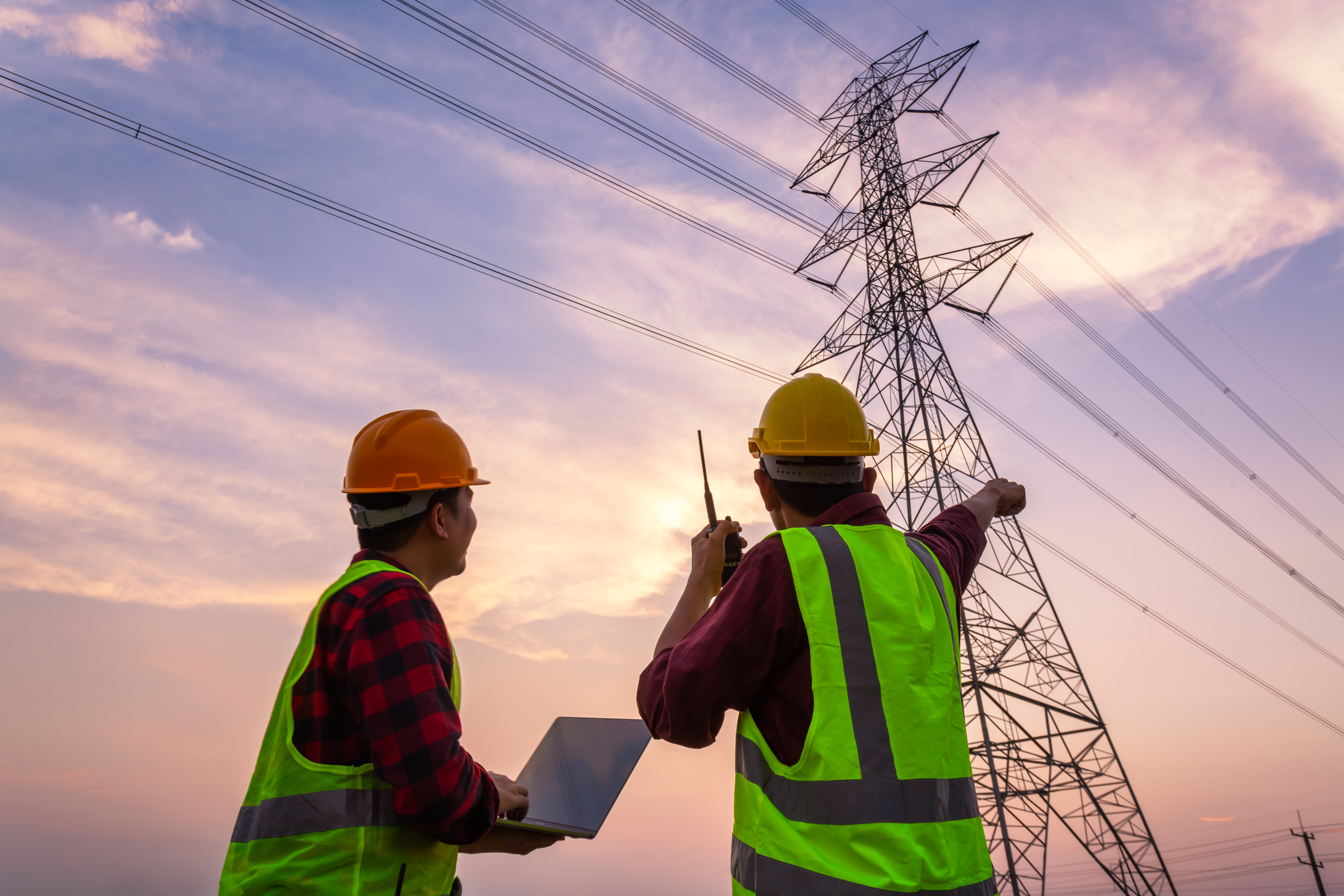 Two workers pointing up towards the sky with electric lines in the background.