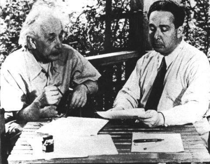 Black and white photo of Albert Einstein sitting at a table, with a letter and pen in front of him.