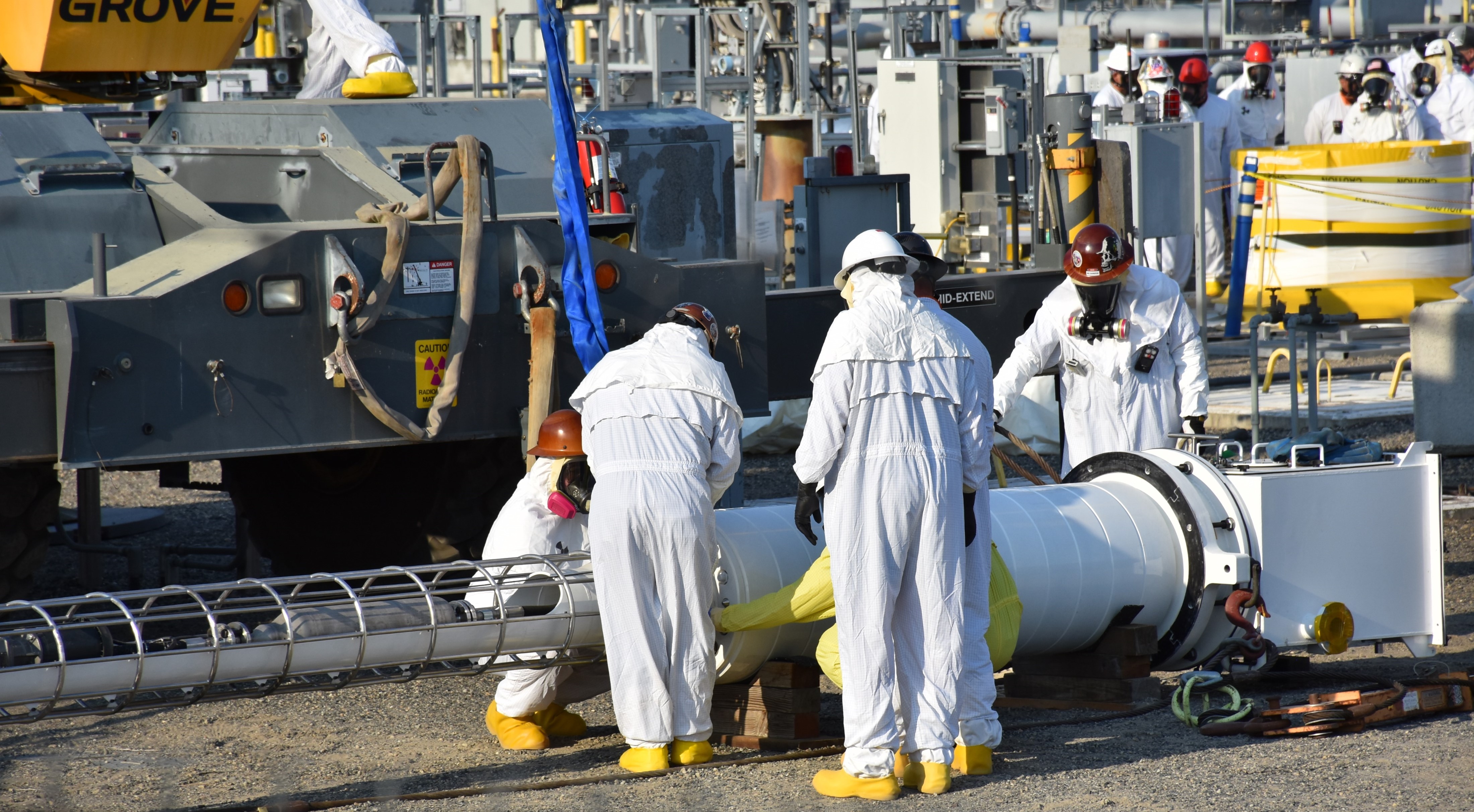 Works in protective clothing huddling around a piece of equipment. 