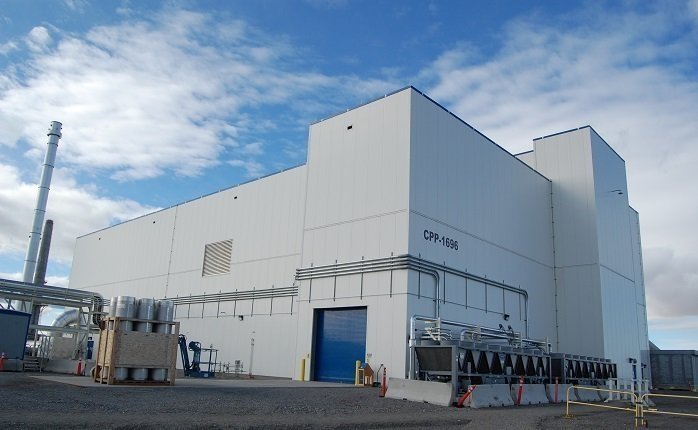 A large white facility building with pipes and machines attached to the outside of it