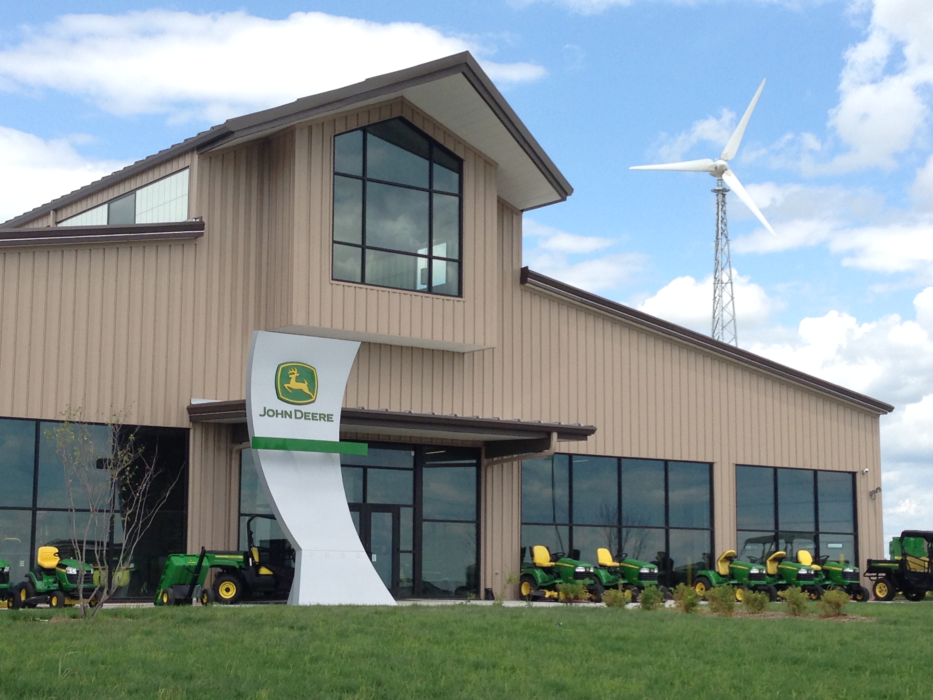 An image of a wind turbine nearby a business with tractors on the grass.