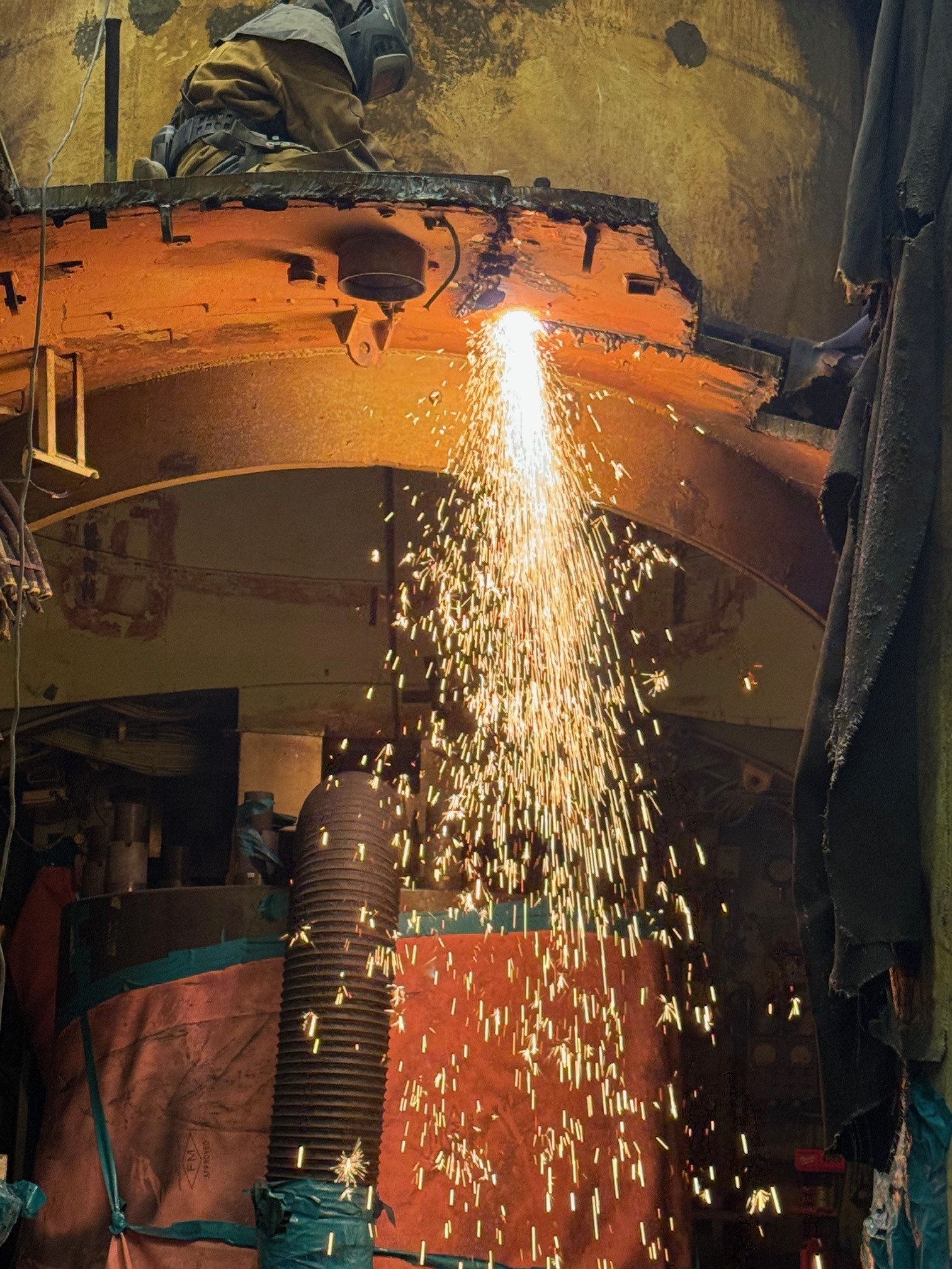 A worker uses a plasma torch to cut through a hull at the S1W prototype.