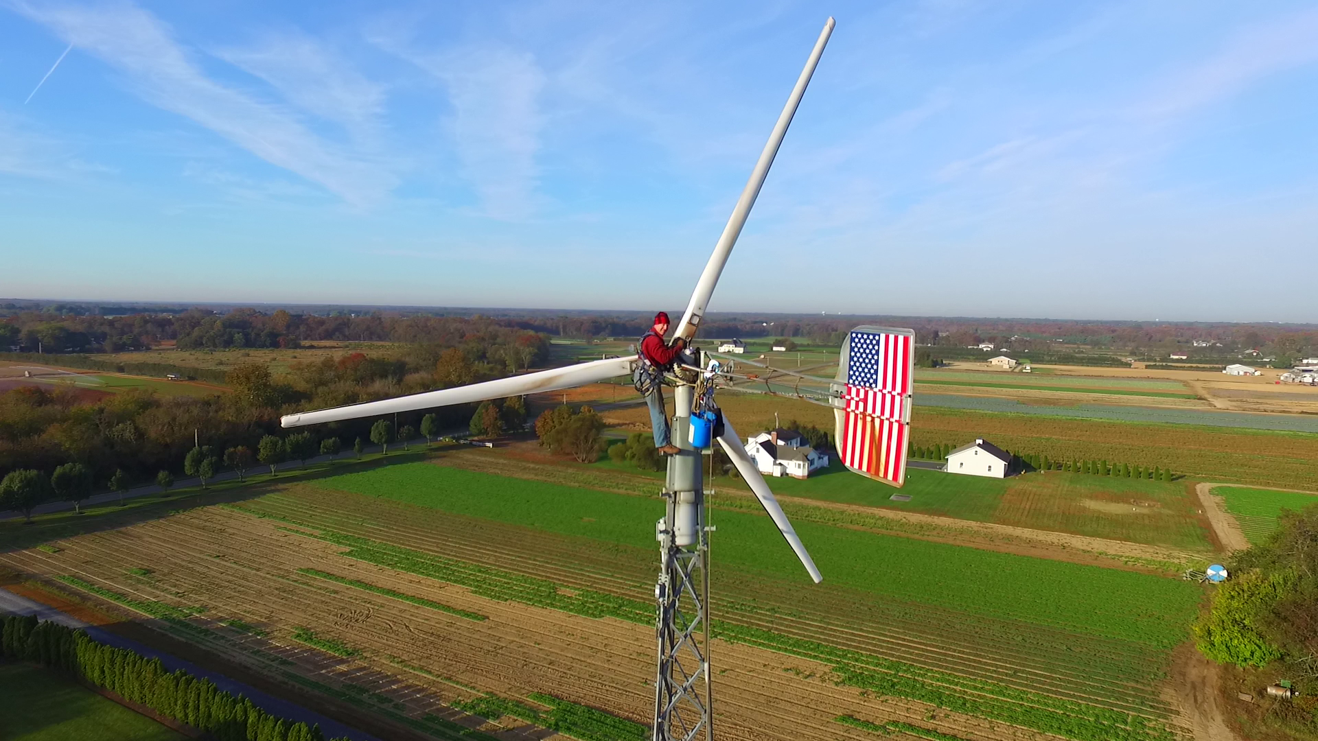 A man works on a wind turbine near a farm