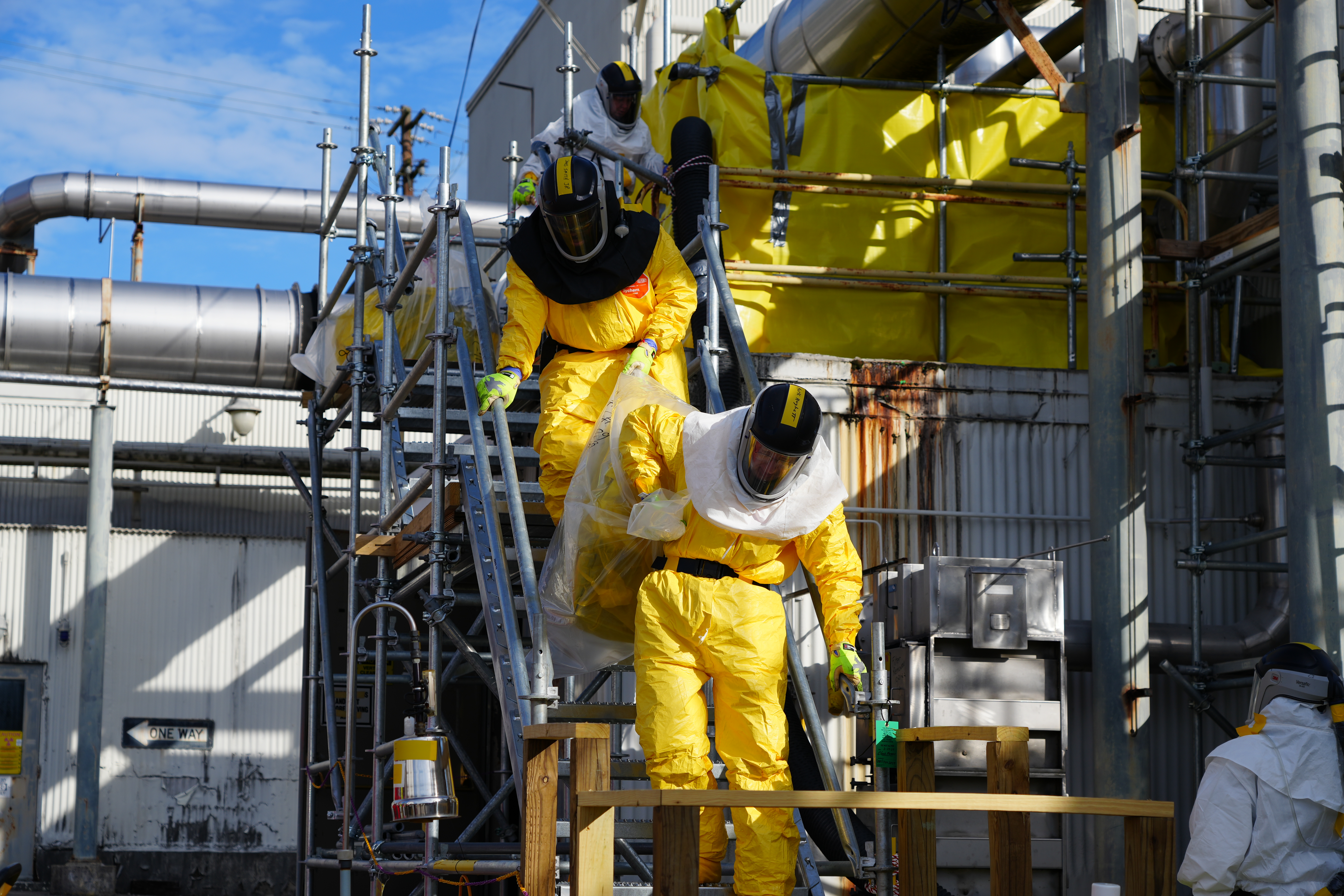 Two employees donning hazmat suits descend outside staircase 