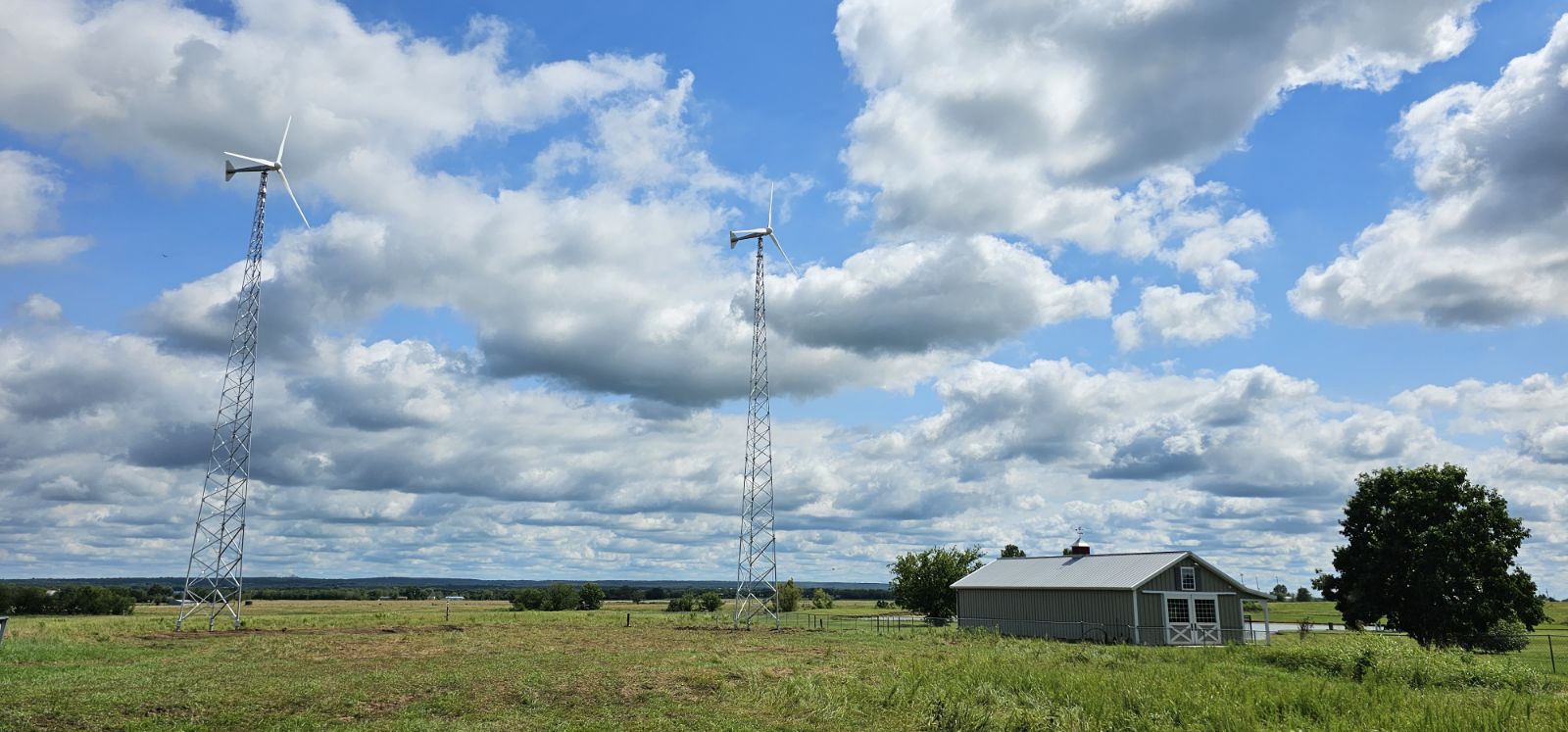 Two wind turbines are in a field surrounded by a farm