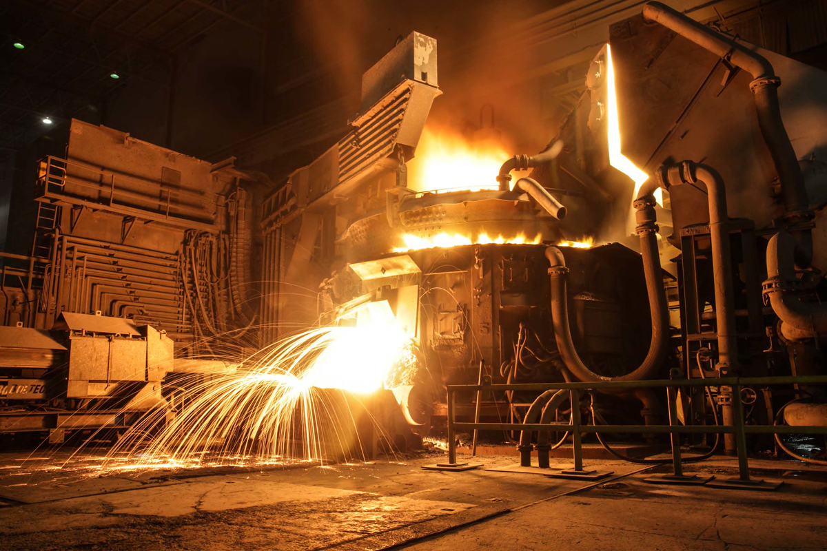 A photo of an electric arc furnace with glowing heat rising up.