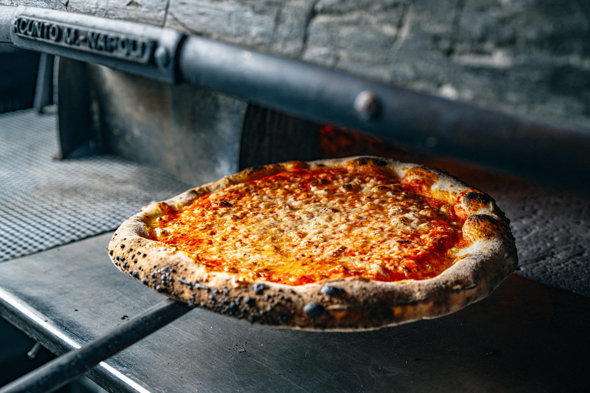 A pizza paddle pulls a cheese pizza out of an oven.