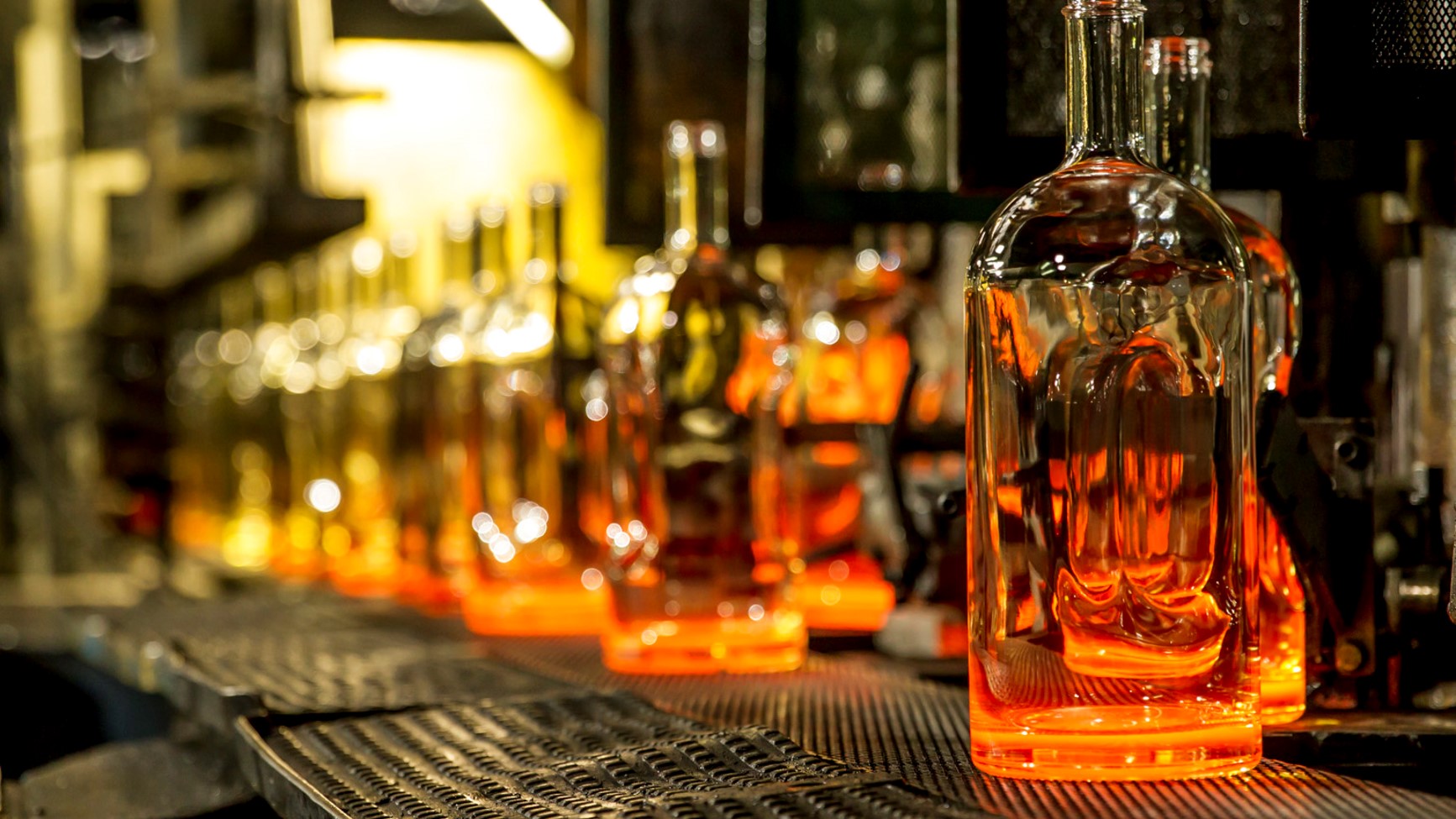 A newly formed glass bottle moves along a conveyor belt at an O-I Glass bottle-making factory