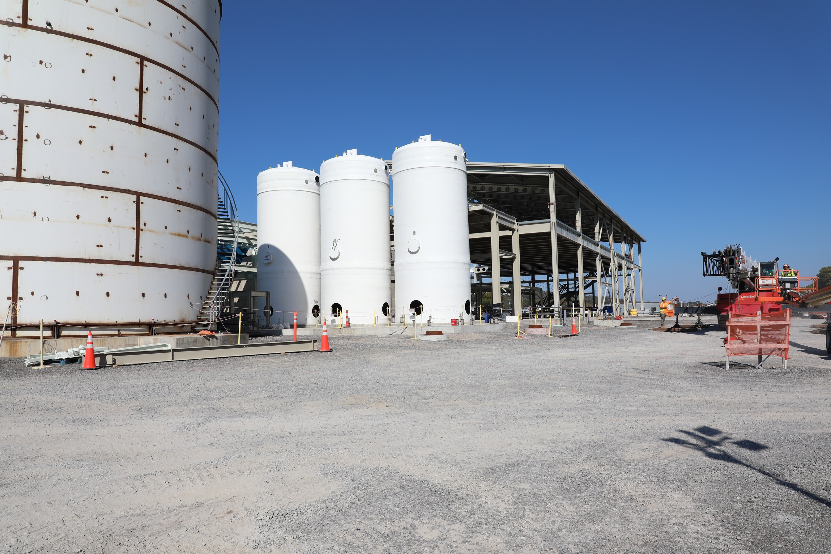 Three large white tanks beside a large white building in a gravel lot