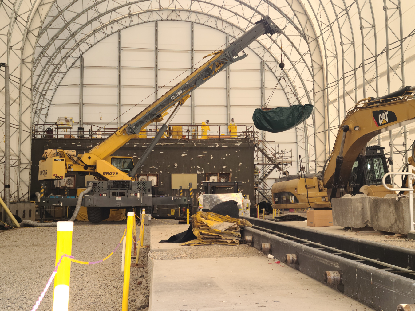 The inside of a facility building with a crane and other work machinery lifting an item