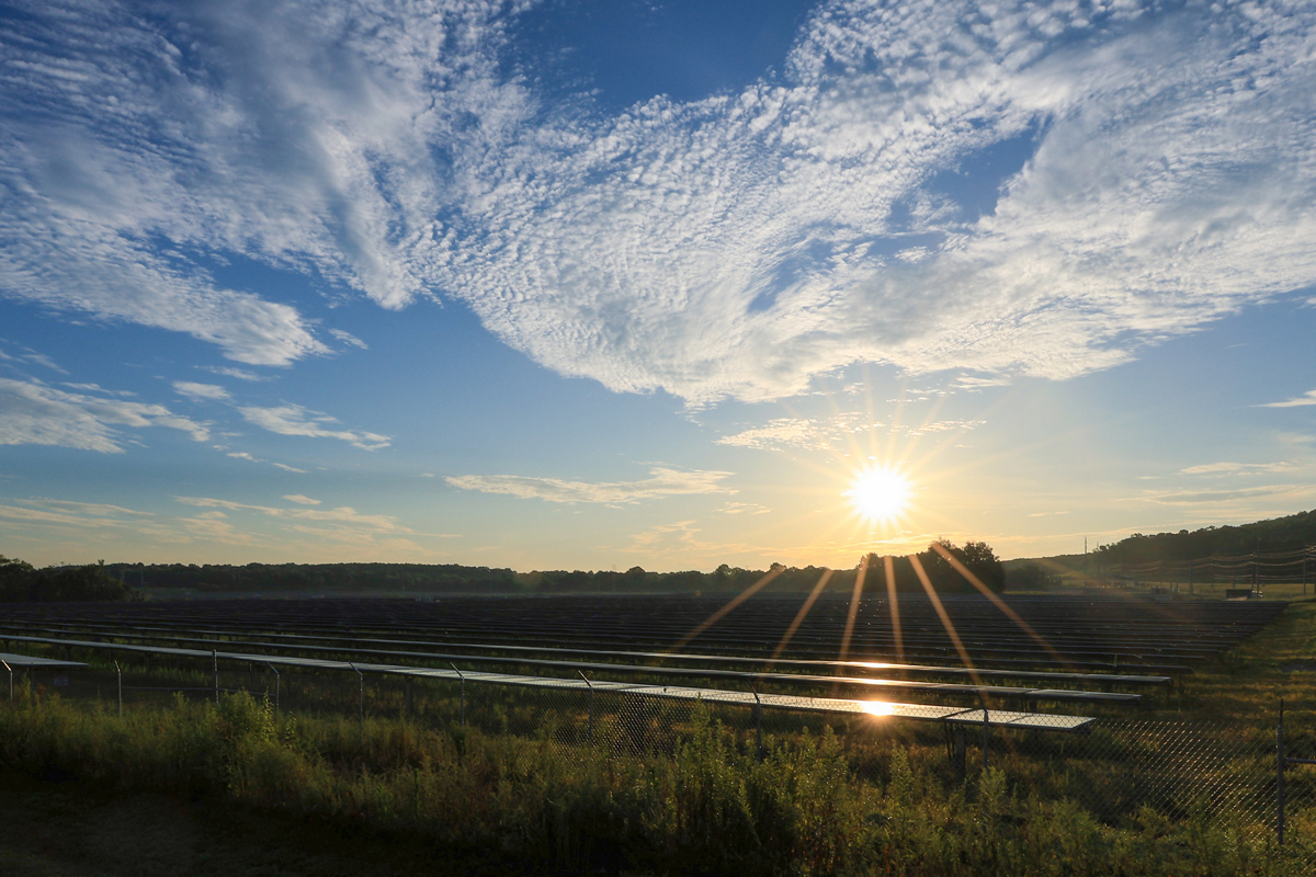 A solar array lit up by a rising sun under a partly cloudy sky.