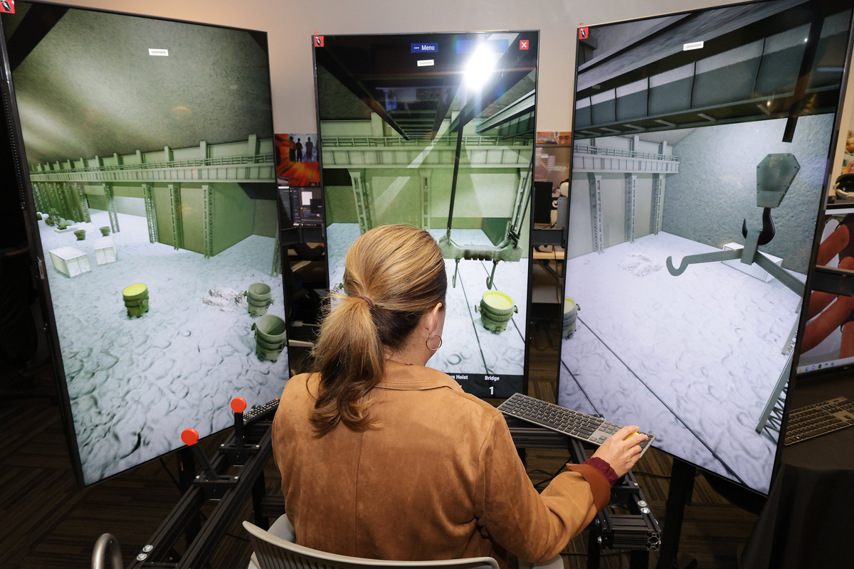 A woman uses a crane training simulation program on three large computer screens.