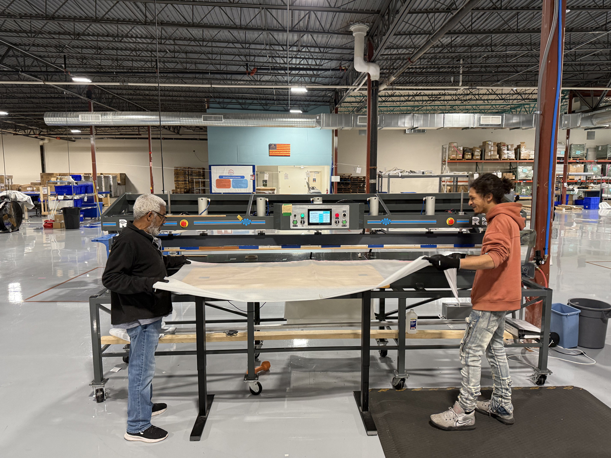 Two workers stretch out a piece of plastic fabric.