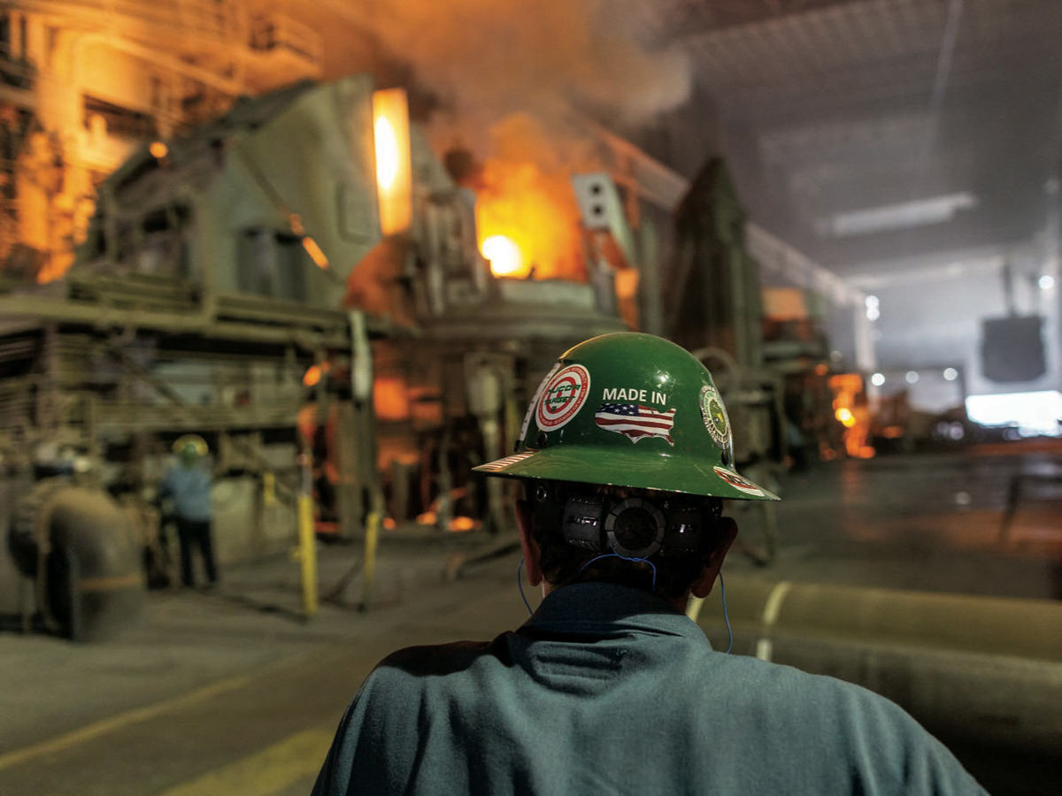 A factory worker in a helmet, photographed from behind.