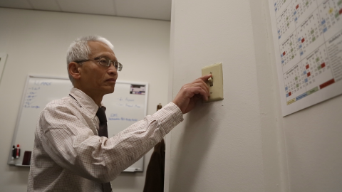 Photo of a man switching on or off a light switch on a wall.