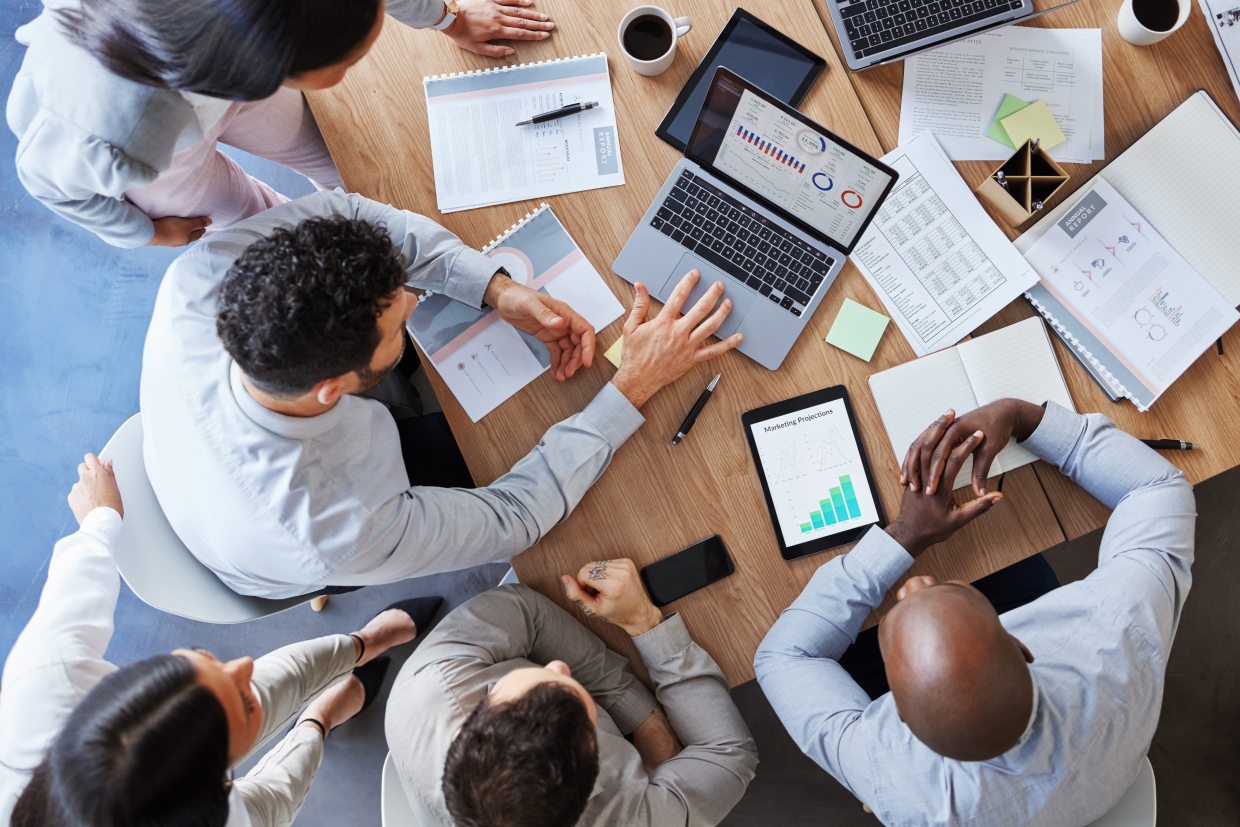 An overhead photo of several people sitting at a table in a meeting.