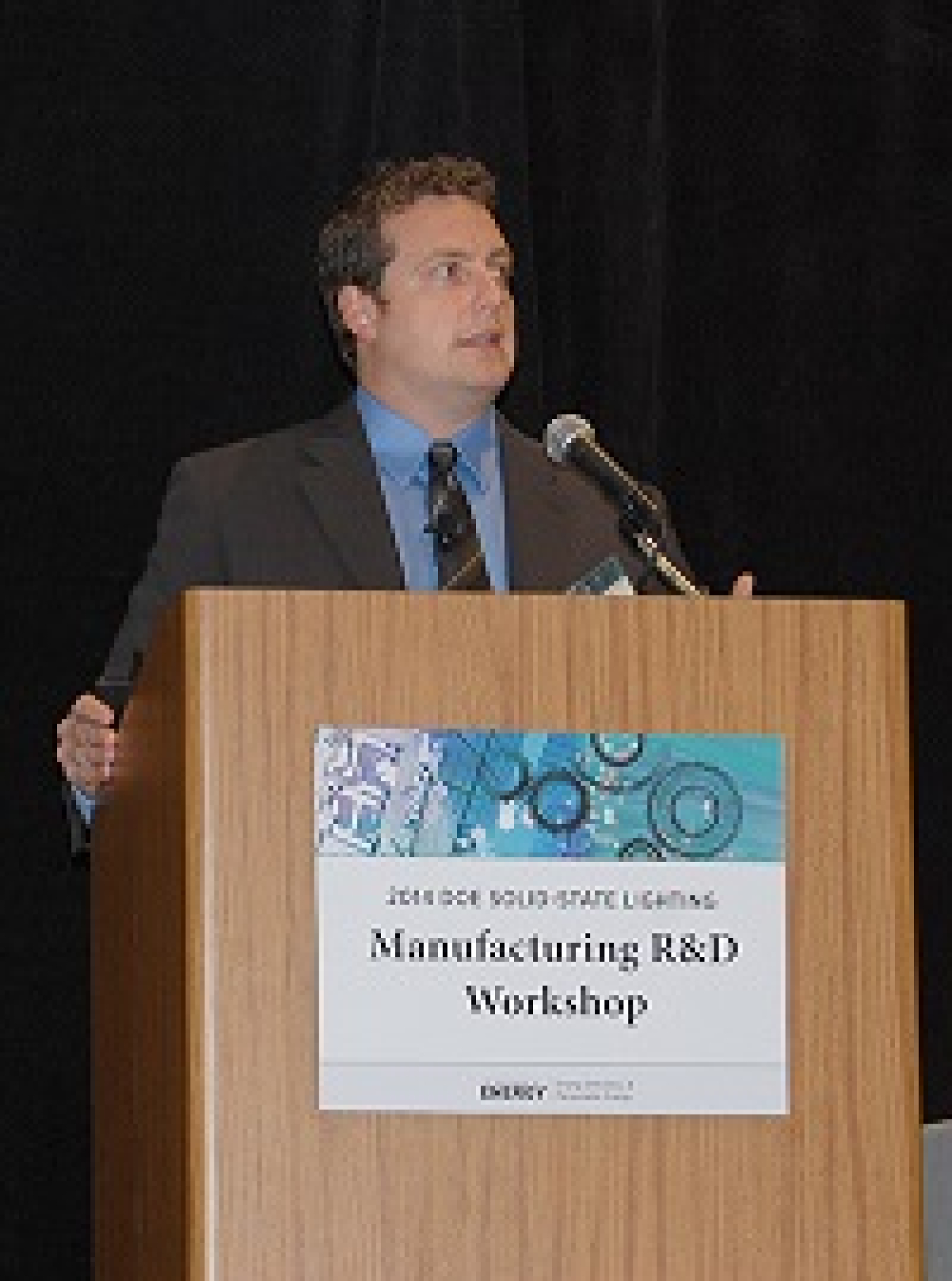 Photo of a man standing behind a podium, talking into a microphone.