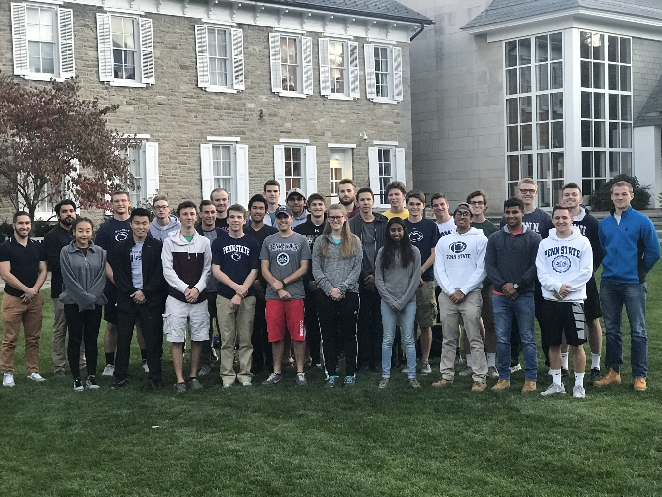 The Pennsylvania State University Collegiate Wind Competition team stands on the grass in front of their university. 