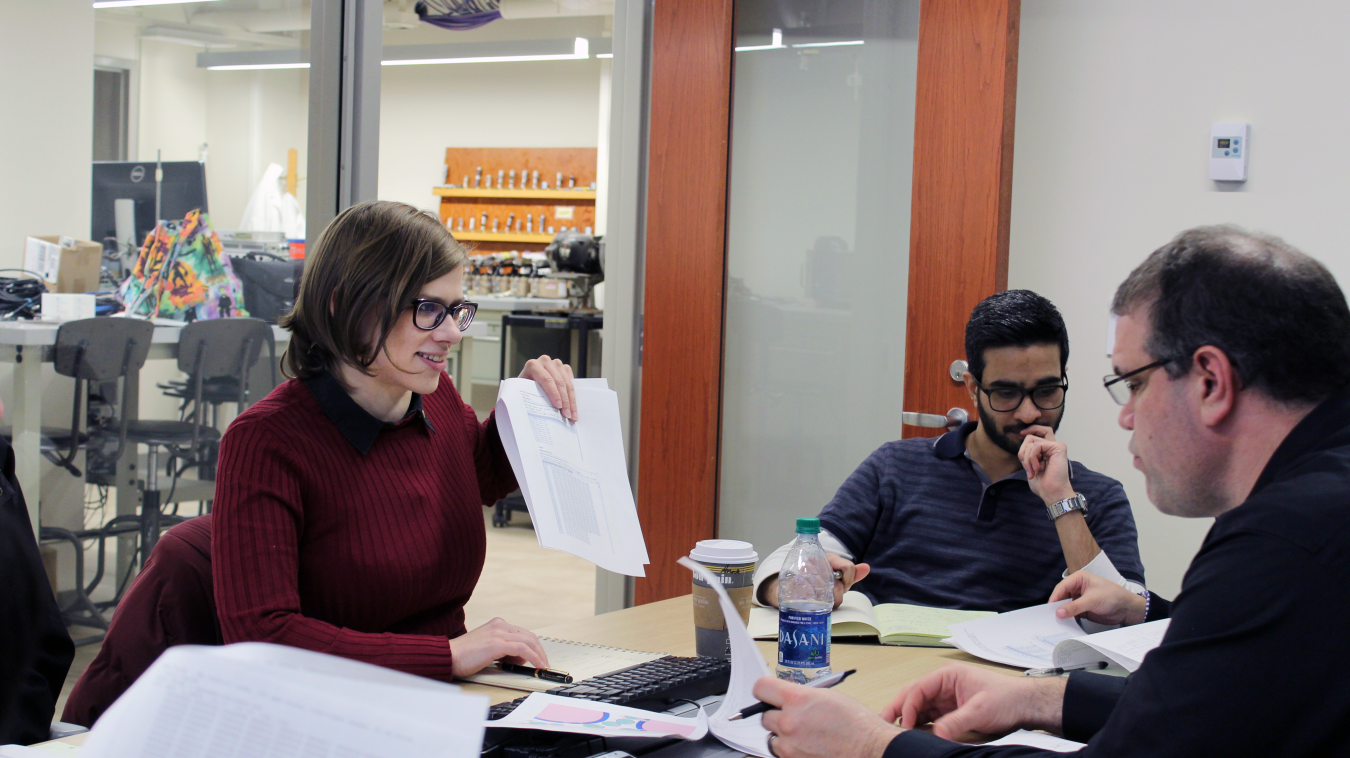 A woman discusses results of a paper she is researching with other students and a professor.