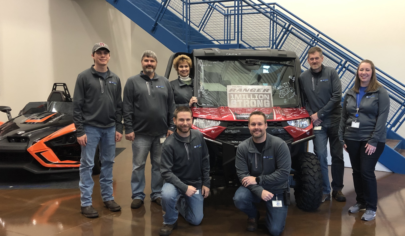 7 people (men and women) standing around an off road vehicle.