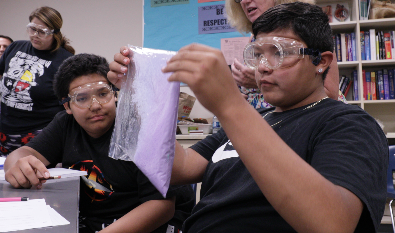 Kids in a classroom wearing safety goggles and examining materials.