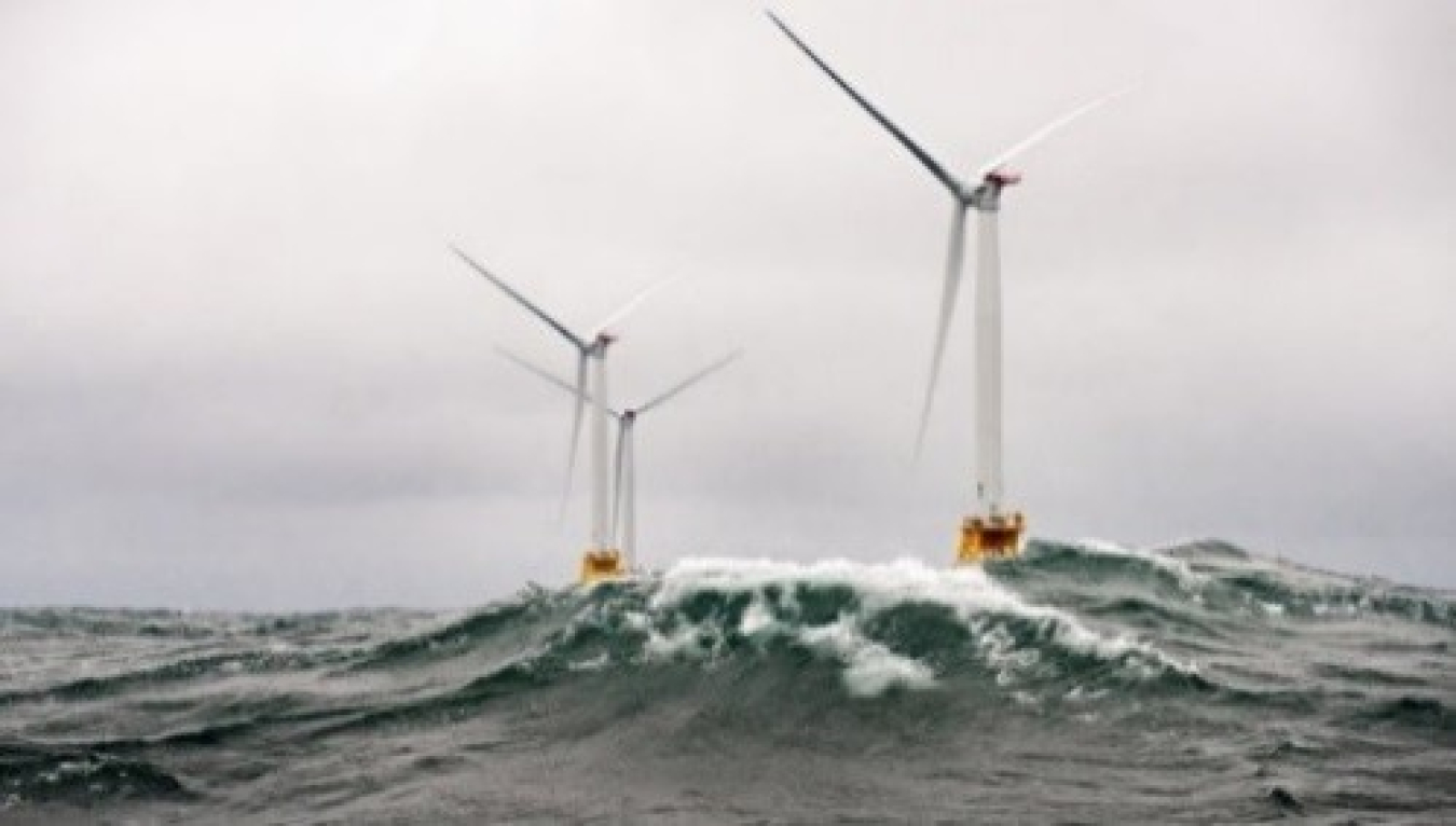 three offshore wind turbines at sea against a grey sky and choppy waves.