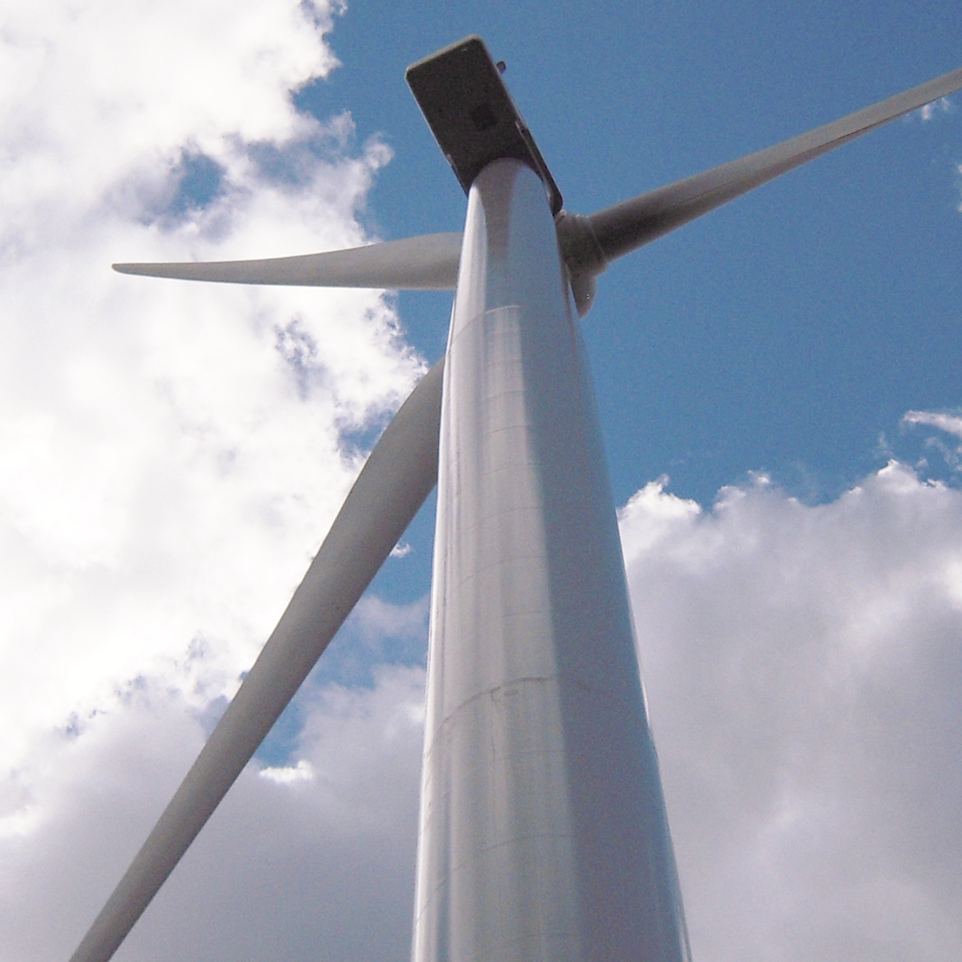 View from below of a wind turbine against a blue sky with some clouds.