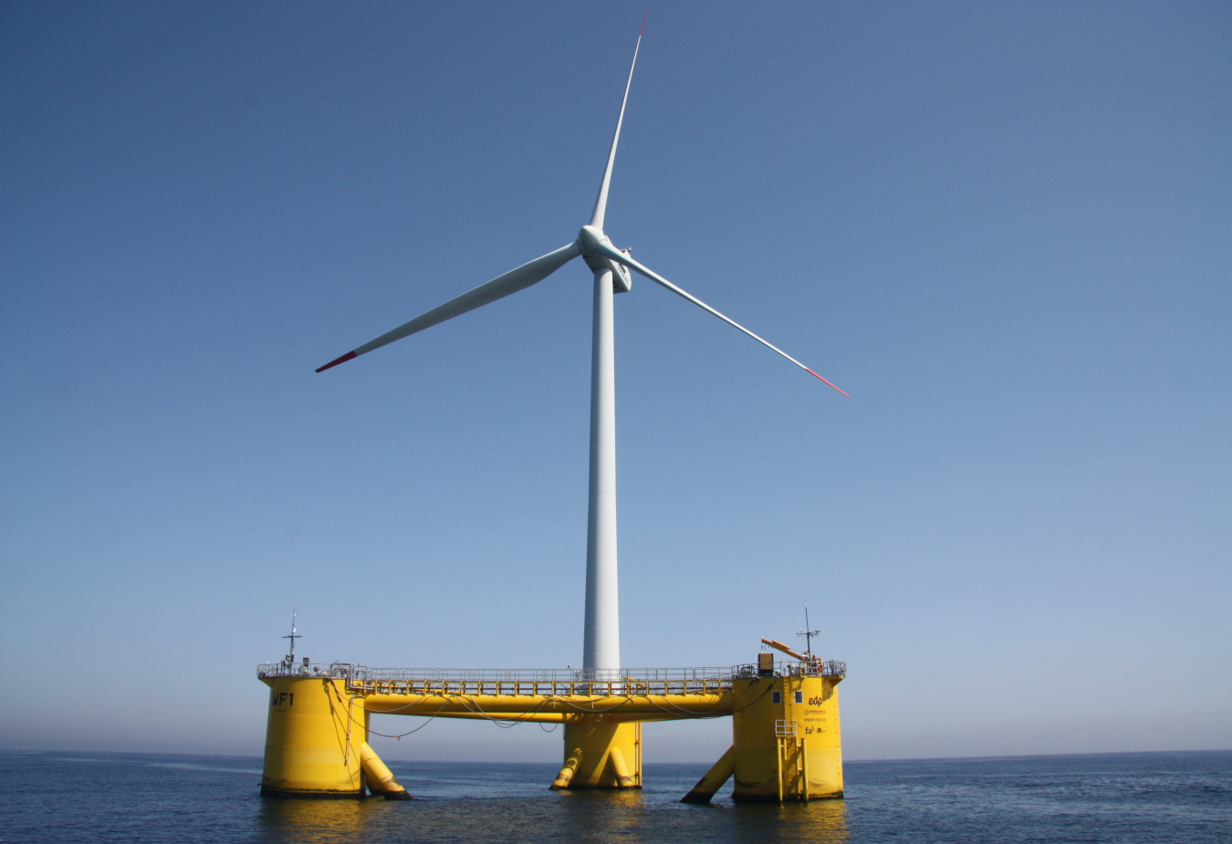 Photo of a wind turbine on a yellow floating platform in the ocean.