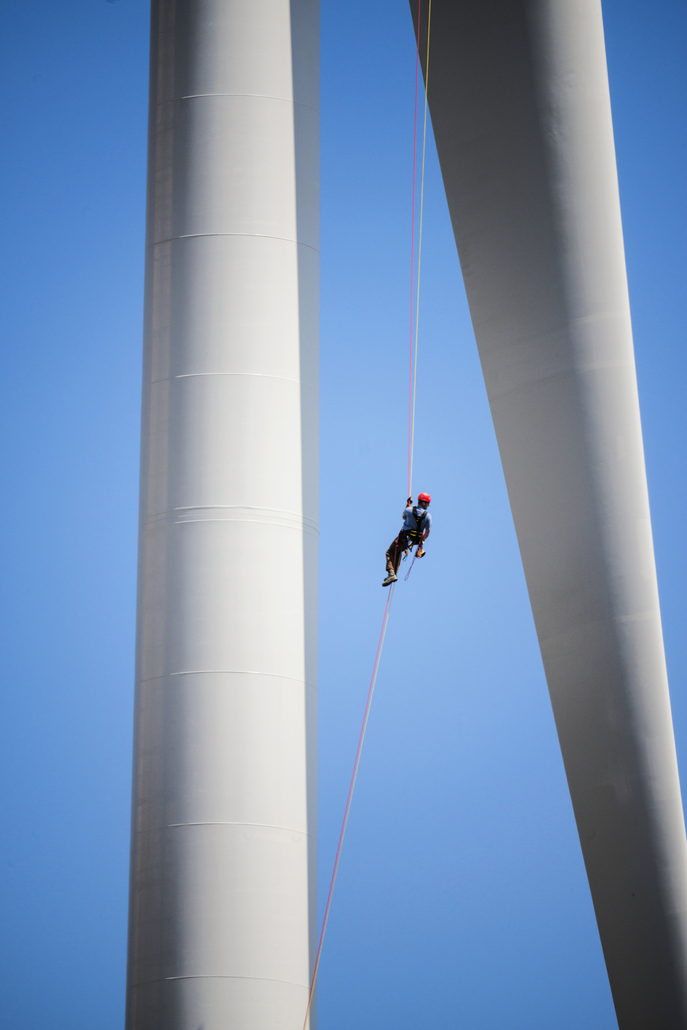 Photo of a wind turbine technician dangling from a rope between two wind turbine blades.