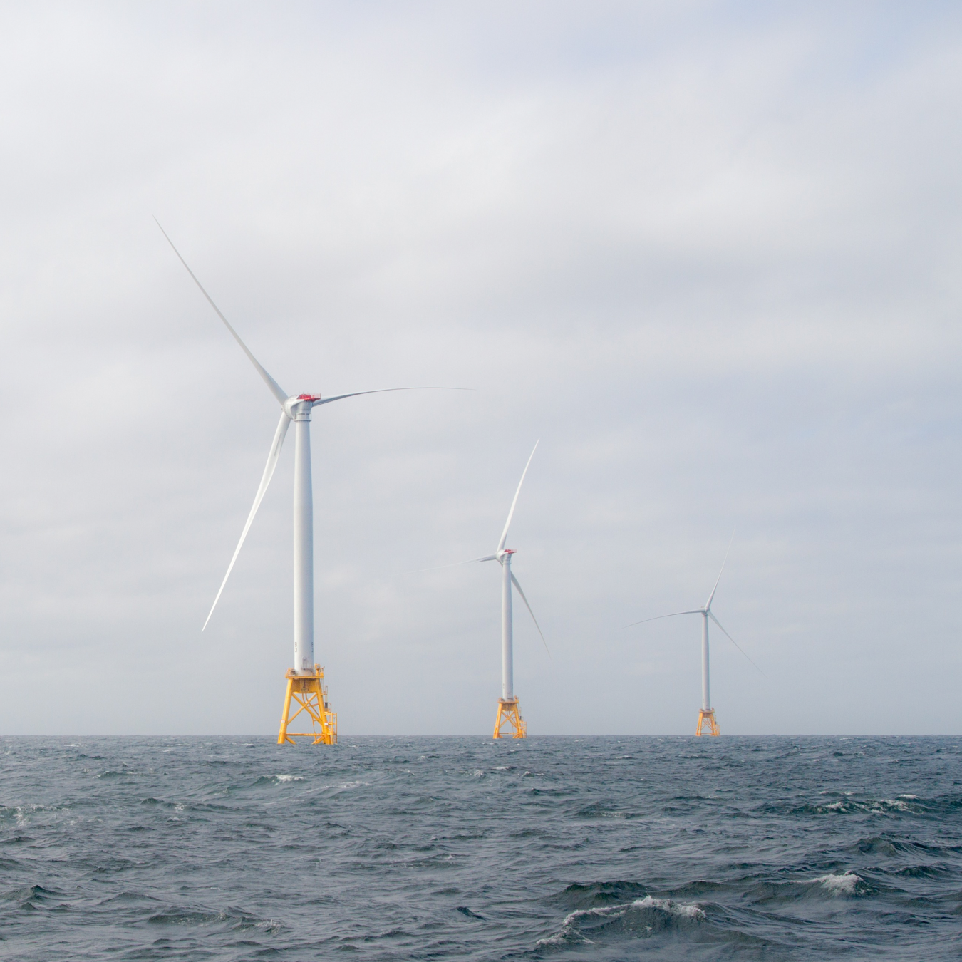 Photo of 4 wind turbines on orange platforms in the middle of ocean.