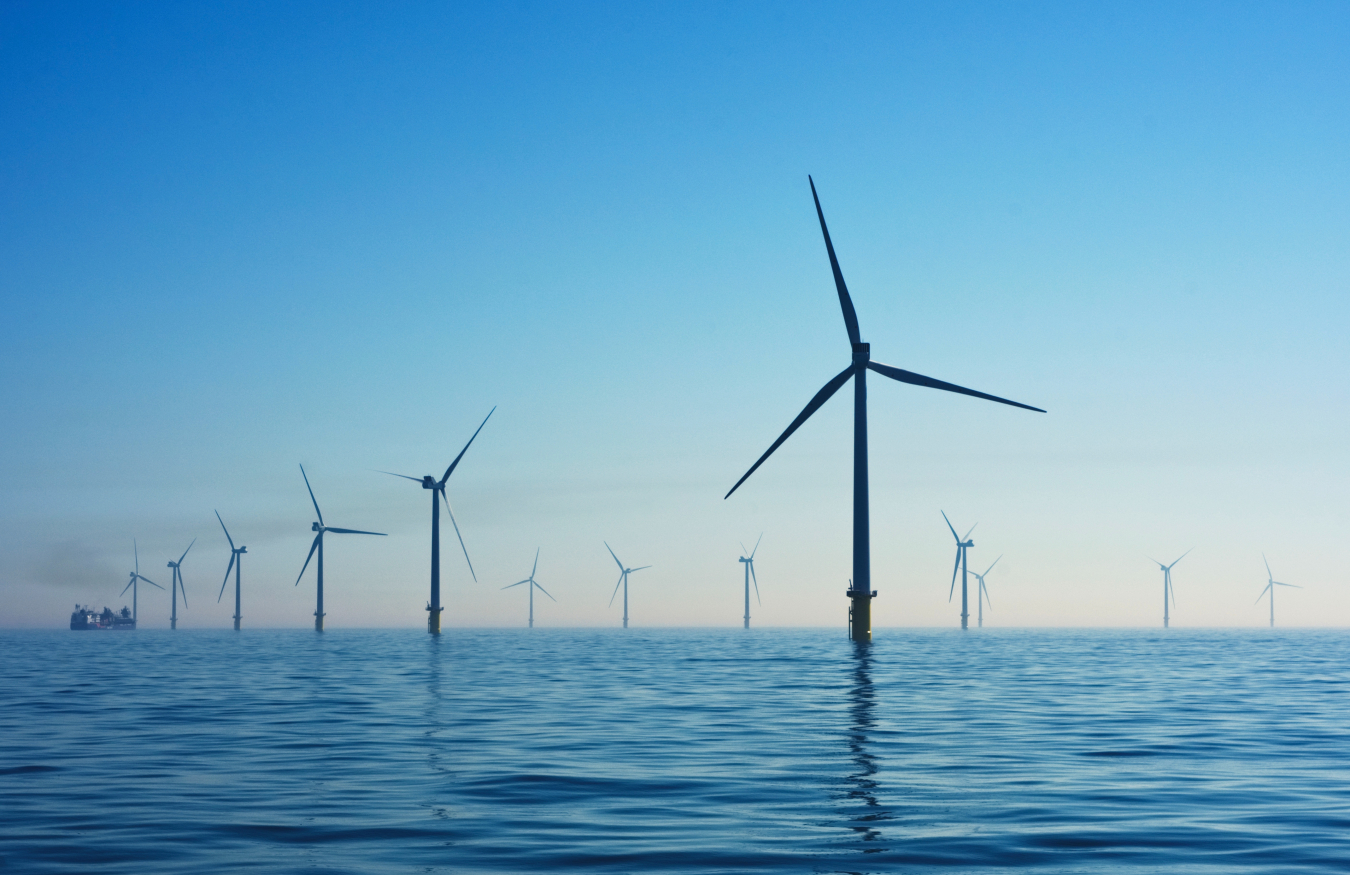 Many wind turbines in ocean and silhouetted against blue sky.