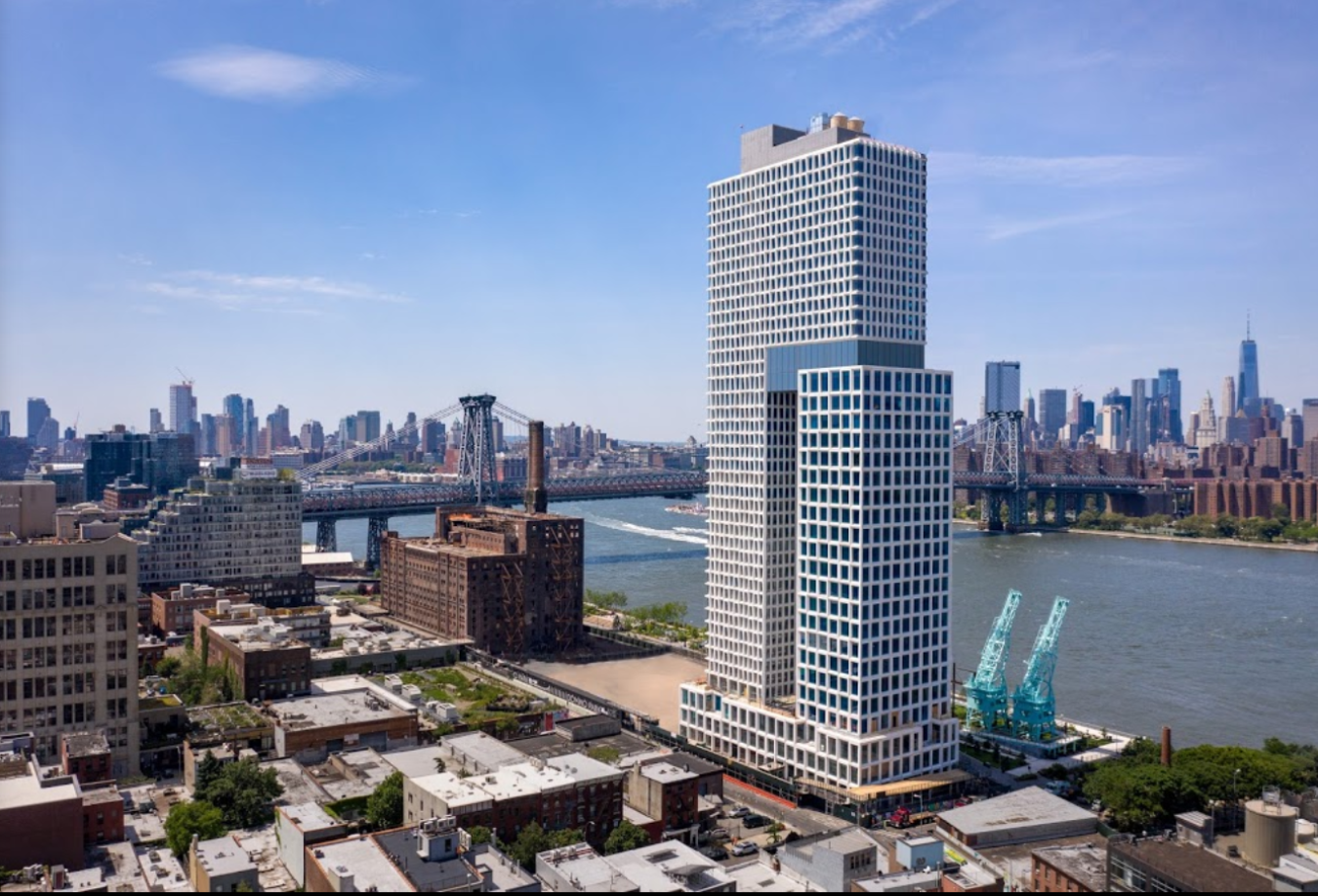 A large overhead view of a stretch of a big city, showing a particularly tall commercial building near a river running through the city, with other buildings all around.