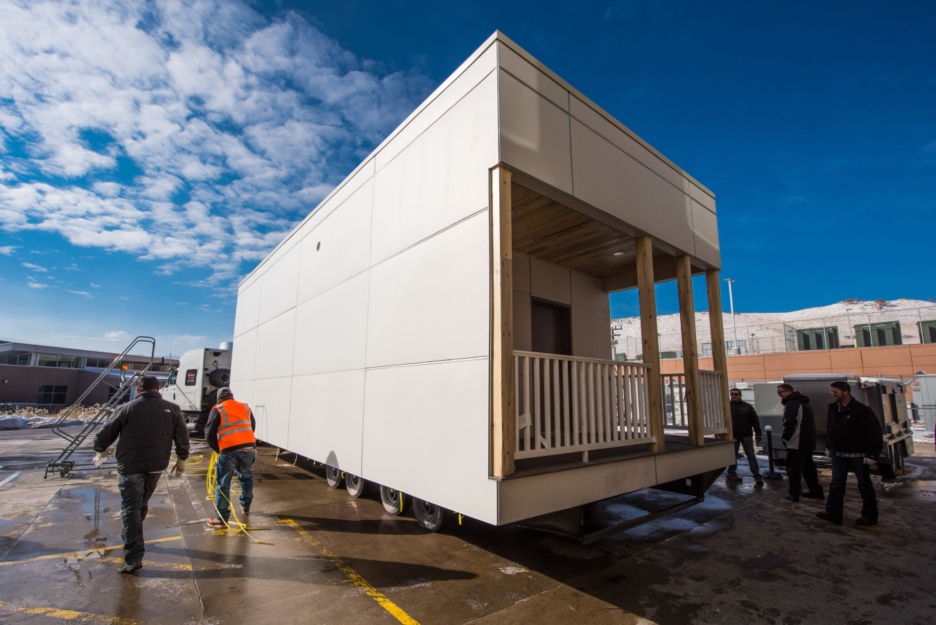 A building unit being moved on wheels, with a few workers standing around it in a parking lot.