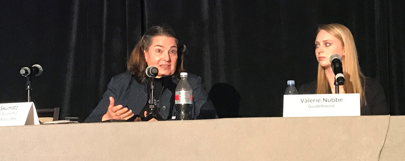 Two women seated at a table on a podium addressing the conference audience.