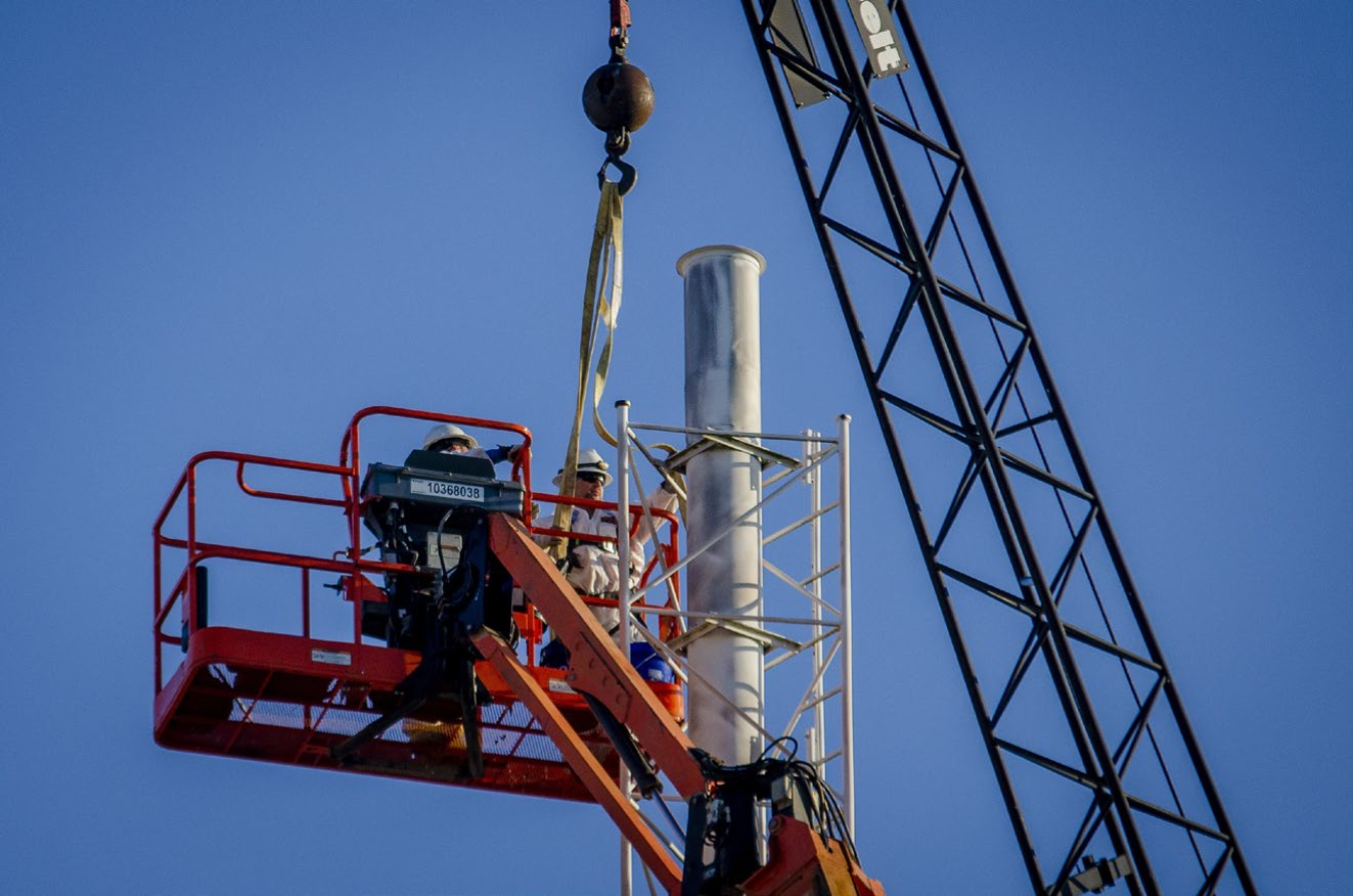 Workers attach a section of the northwest stack to a crane to be hoisted away and dismantled. Both the northwest and southwest stacks on the west side of the C-400 Building have been removed.