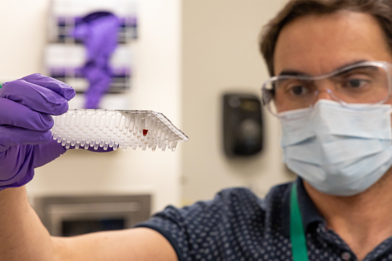 Man in a face mask and goggles holding up a plastic apparatus for holding samples.