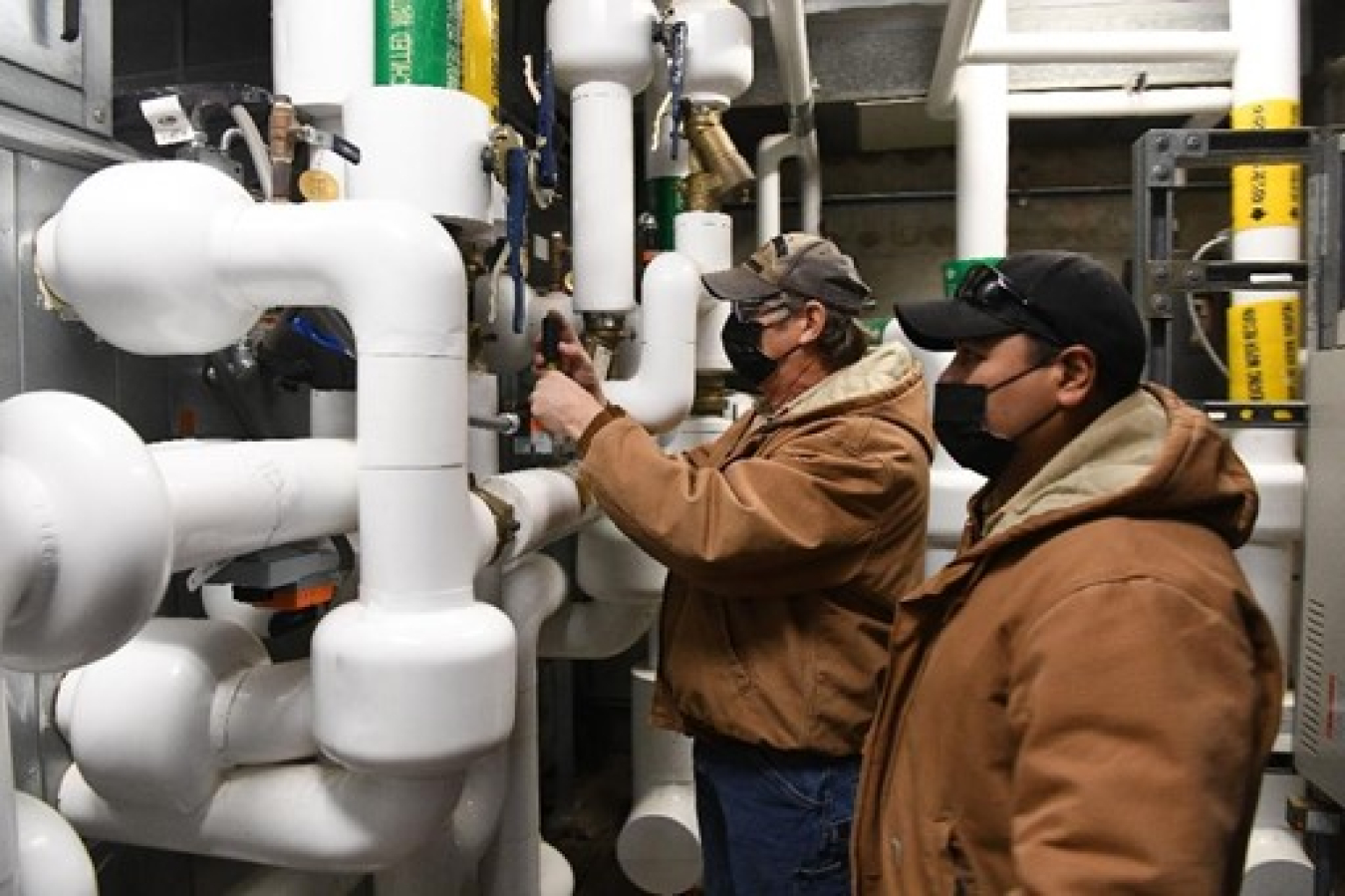 Instrument technicians adjusting hot water controls in an equipment room at the Pantex Plant.