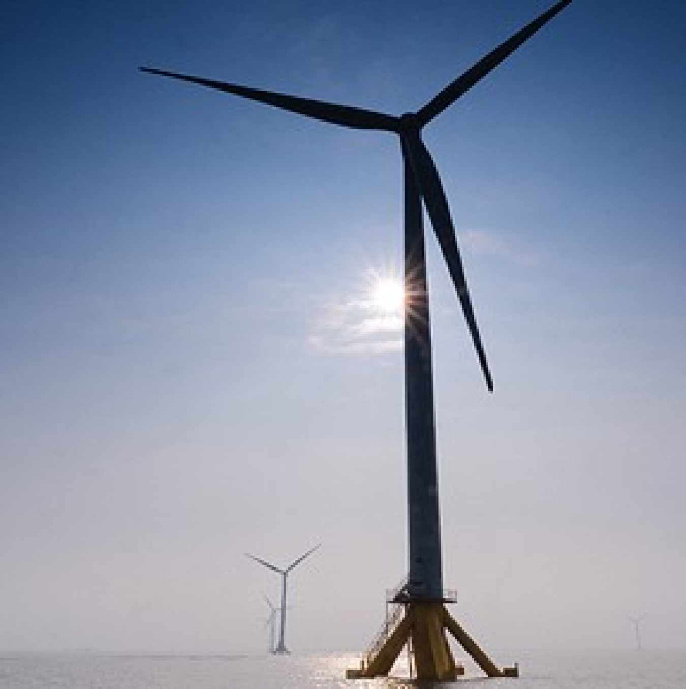 Offshore wind turbines at sea with sun shining.