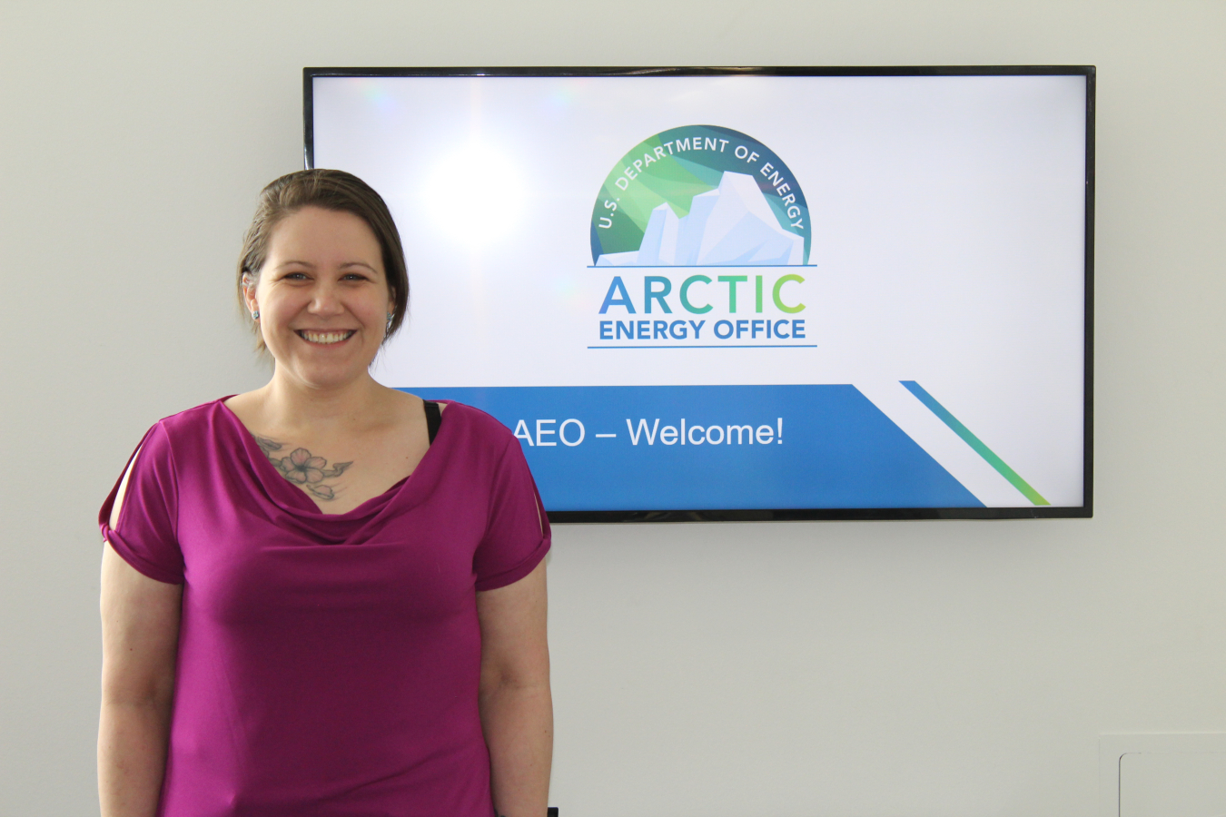 Head and shoulders photo of Nicole Jacobs standing in front of the Arctic Energy Ofice logo on a white board. 