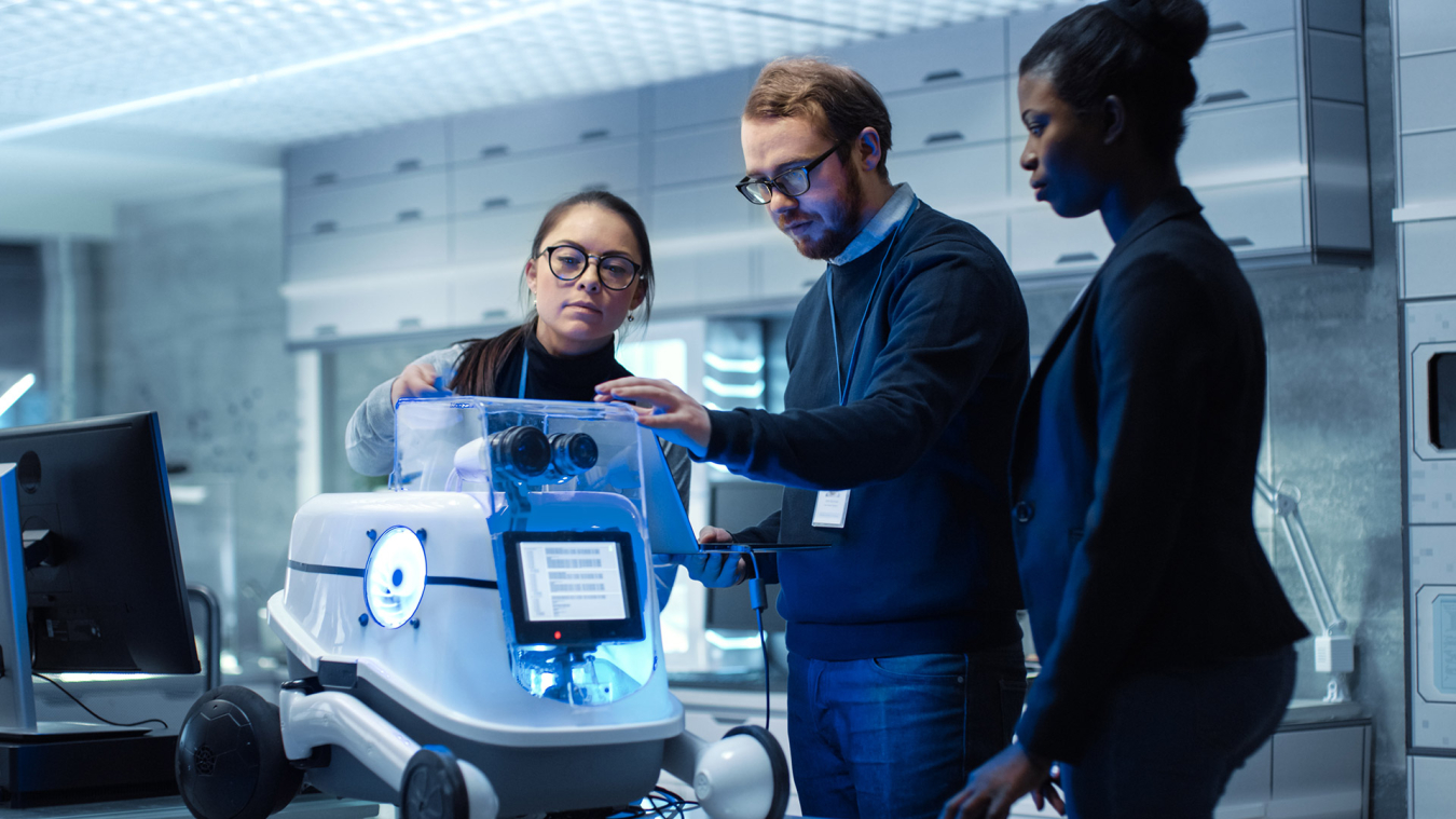 Three people standing behind a machine connected to a laptop.