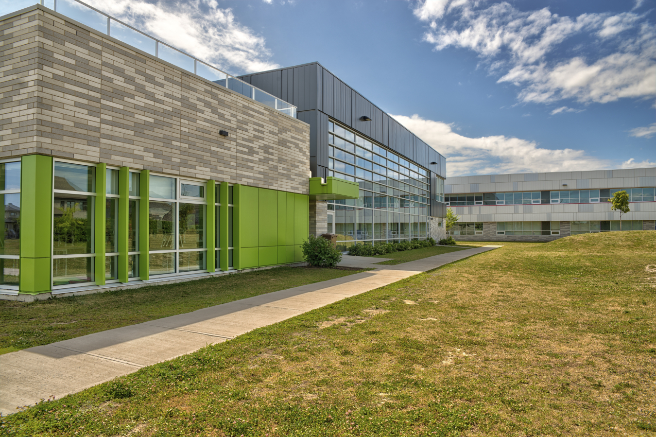 Exterior photo of a school building, with two different design sections shown on one side, and a sidewalk next to it.