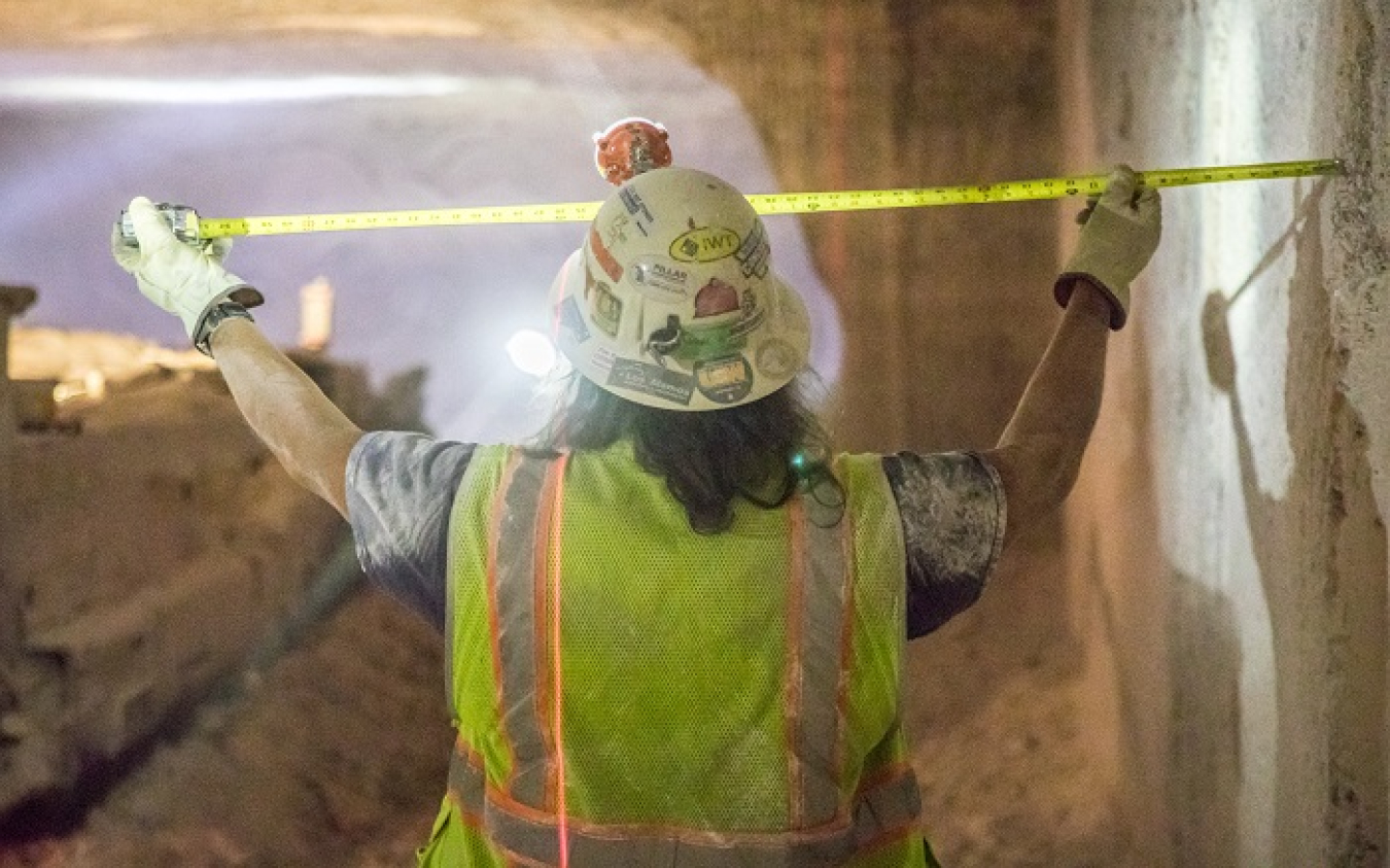 With a red laser measurement line showing on the wall ahead of him, Waste Isolation Pilot Plant underground miner Blas Castaneda uses a tape measure to check dimensions in Panel 8’s Room 7. Rooms where transuranic waste is emplaced are 300 feet long, 33 feet wide, and 15 feet high. Panel 8 mining totaled more than 157,000 tons of mined salt.