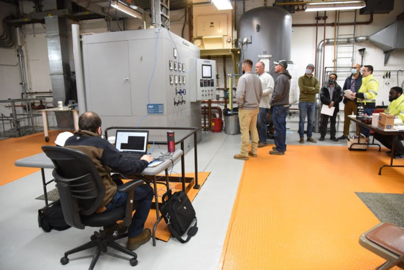 People gather around large gray devices called ultracapacitors that are designed to store and deliver energy quickly.