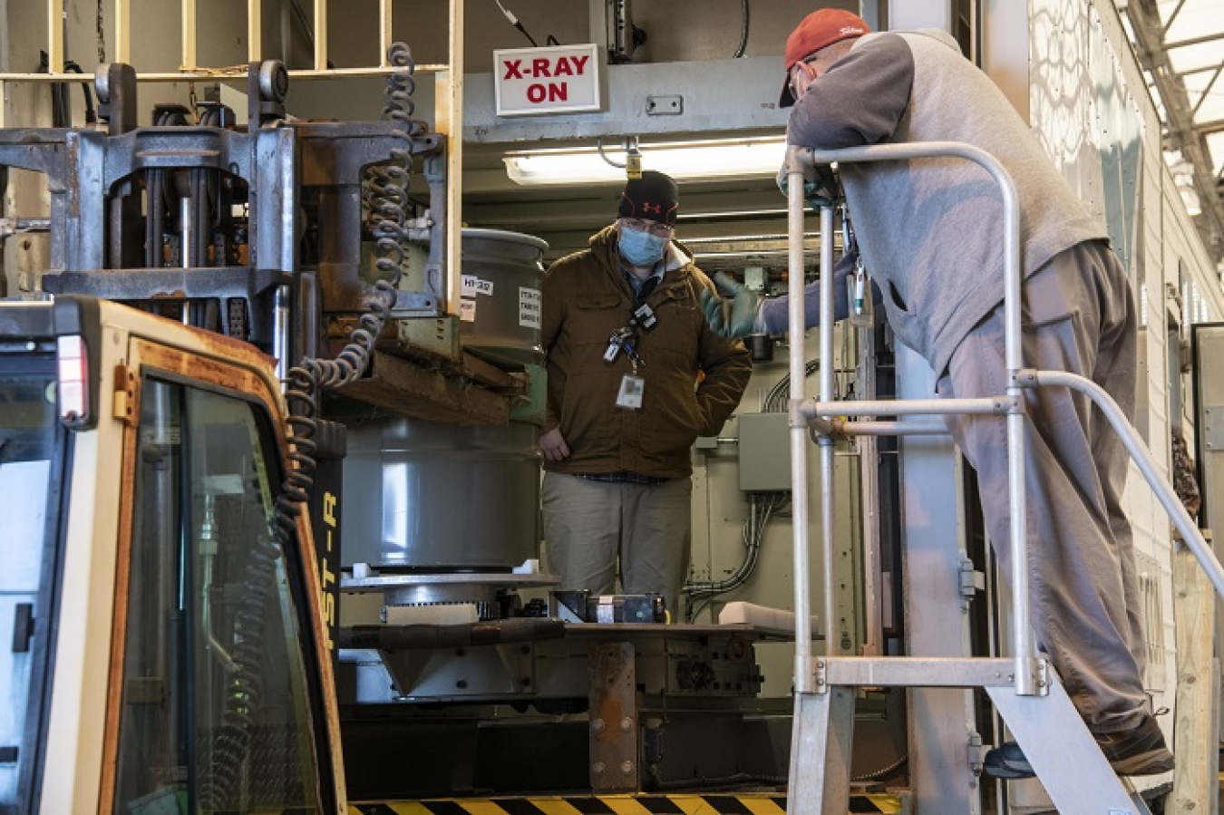 DOE Central Characterization Project subcontractor Tyler Watson, left, and Savannah River Nuclear Solutions Operator Norman Sykes load a transuranic waste drum into a real-time radiography unit for characterization at the Solid Waste Management Facility at the Savannah River Site.