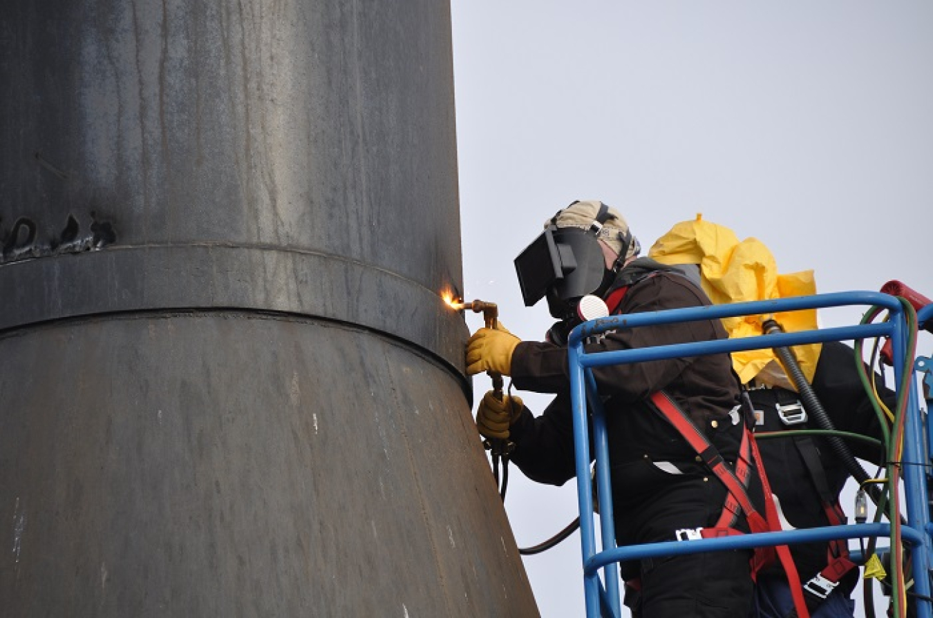 Mike Peterson, a journeyman pipefitter with EM contractor Central Plateau Cleanup Company, uses a torch to cut through one of three 50-foot-tall ventilation stacks, part of the demolition of an old boiler building that supported the K West Reactor during Hanford Site operations.