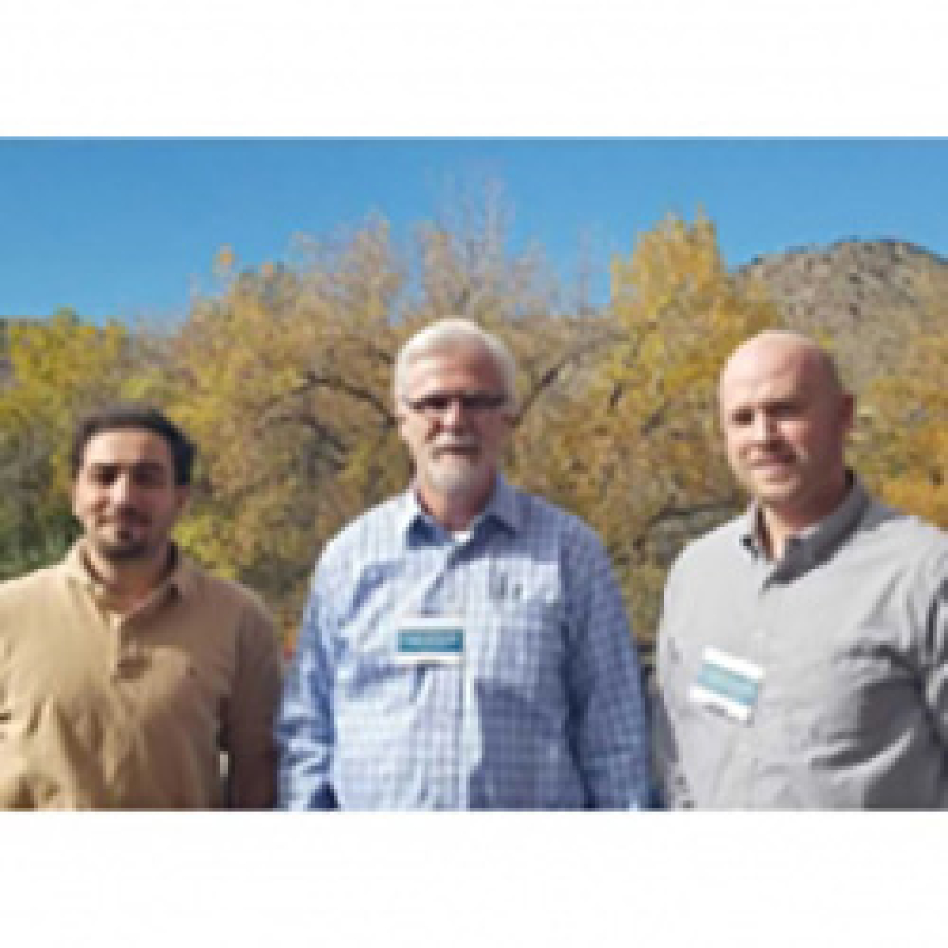 Three men smiling while standing outside.